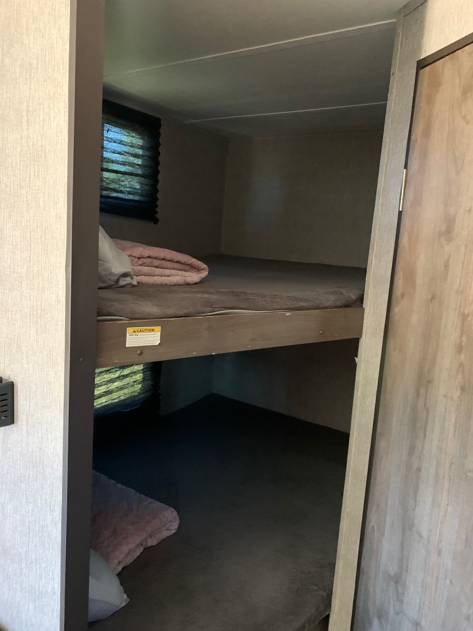 Cozy bunk beds in an RV rental, with grey mattresses, pink blankets, and a window with blinds. Perfect for travel.. Dutchman Coleman Lantern LT 2020