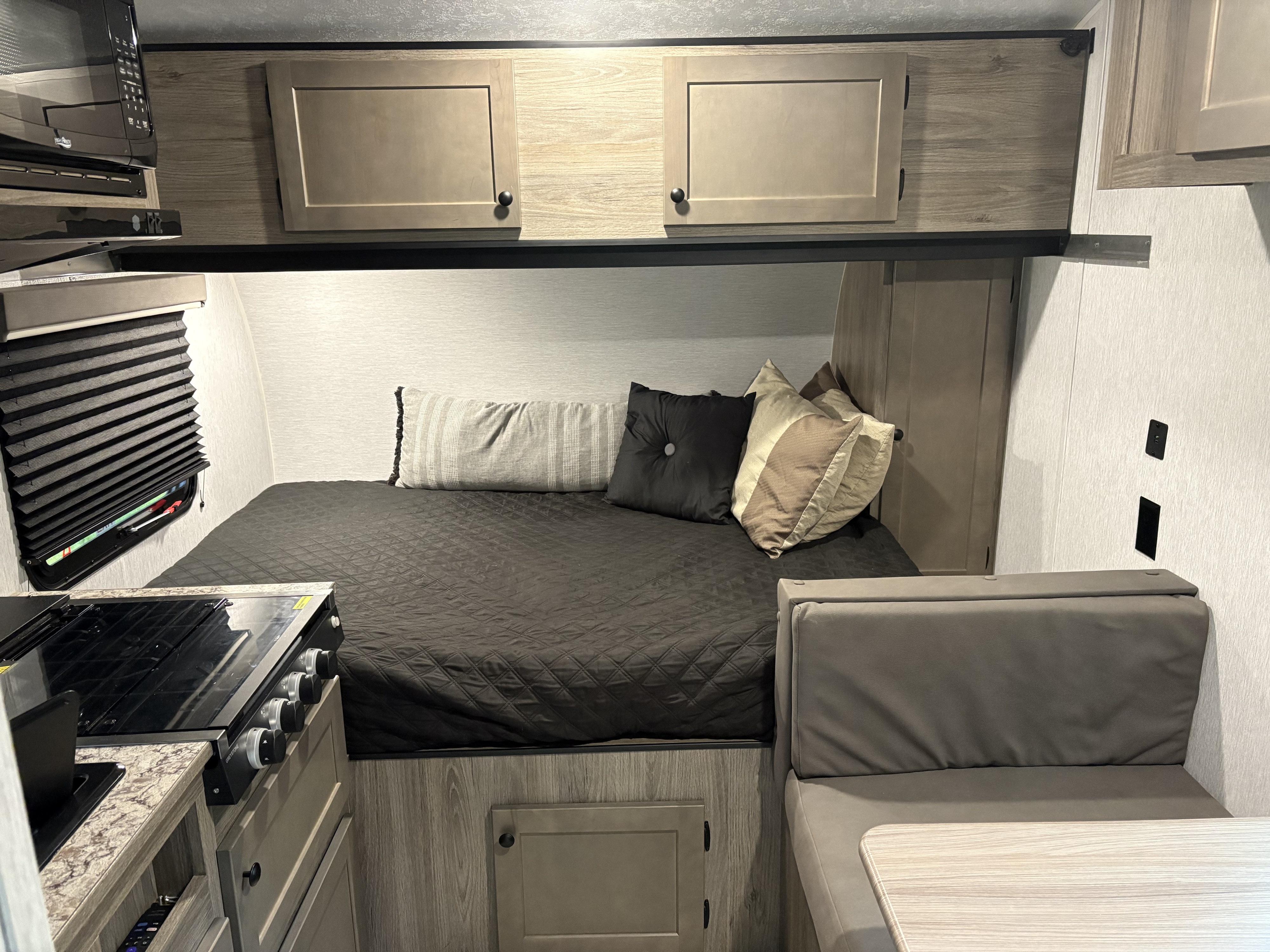 RV rental interior: A cozy bedroom with a dark quilted bed, practical kitchen with stove, and comfortable dinette area.. Sunset Park RV SunLite 16BH 2025
