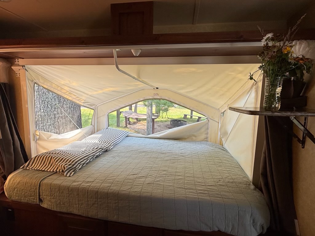 Cozy RV rental pop-out bedroom with a comfortable bed and peaceful campsite view, perfect for camping travel.. Forest River Rockwood Roo 2011