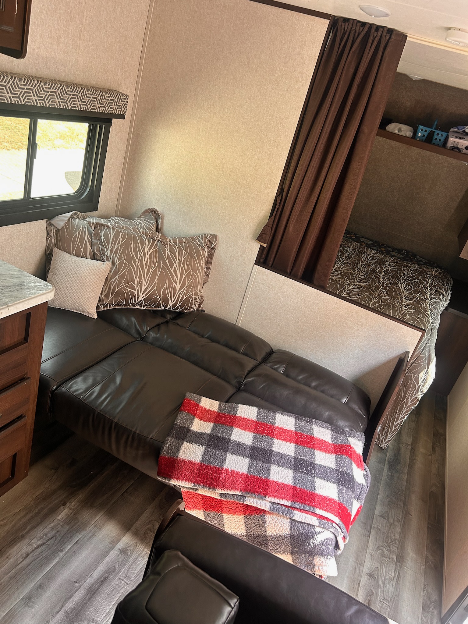 Comfortable RV rental interior: leather couch with plaid blanket and patterned pillows, leading to a curtained bunk bed.. Jayco Jay Flight 2019