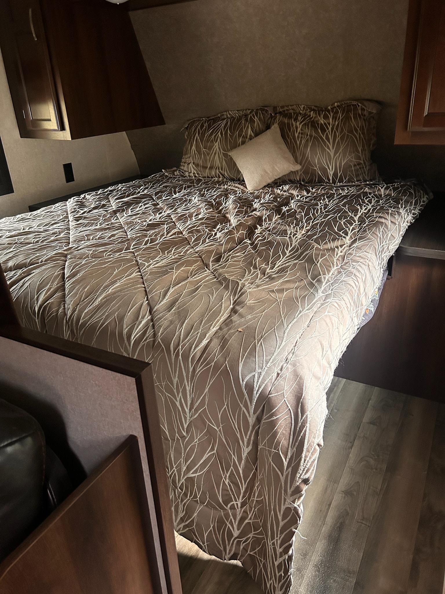 Cozy RV rental bedroom with a brown and white tree-patterned bed, dark wood cabinetry, and laminate flooring.. Jayco Jay Flight 2019