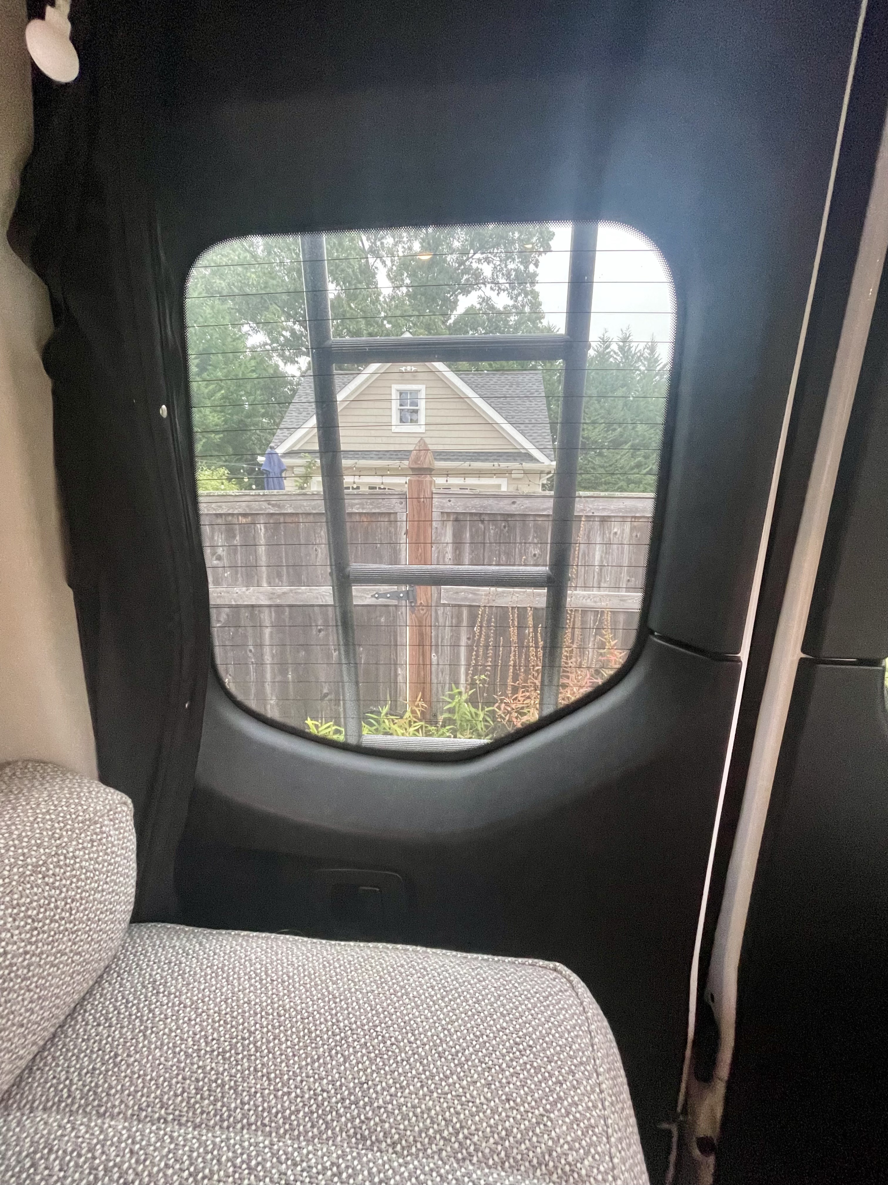 Inside an RV rental, a cozy seat offers a view through the back window of a house, fence, and rear ladder.. Winnebago Boldt 2022