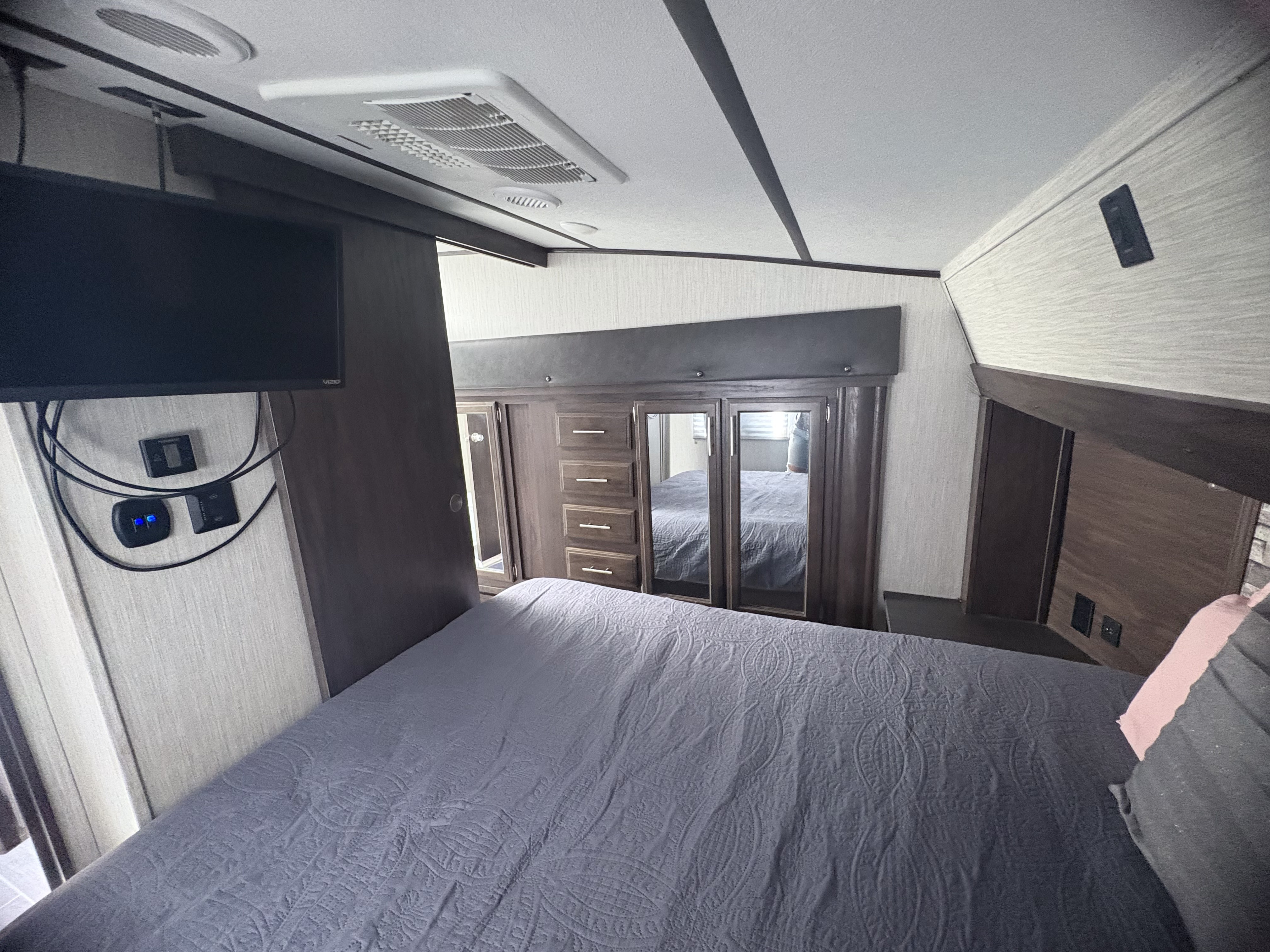 This RV rental bedroom offers a gray quilted bed, TV, and clever mirrored storage, maximizing space for travelers.. Forest River Arctic wolf 2020