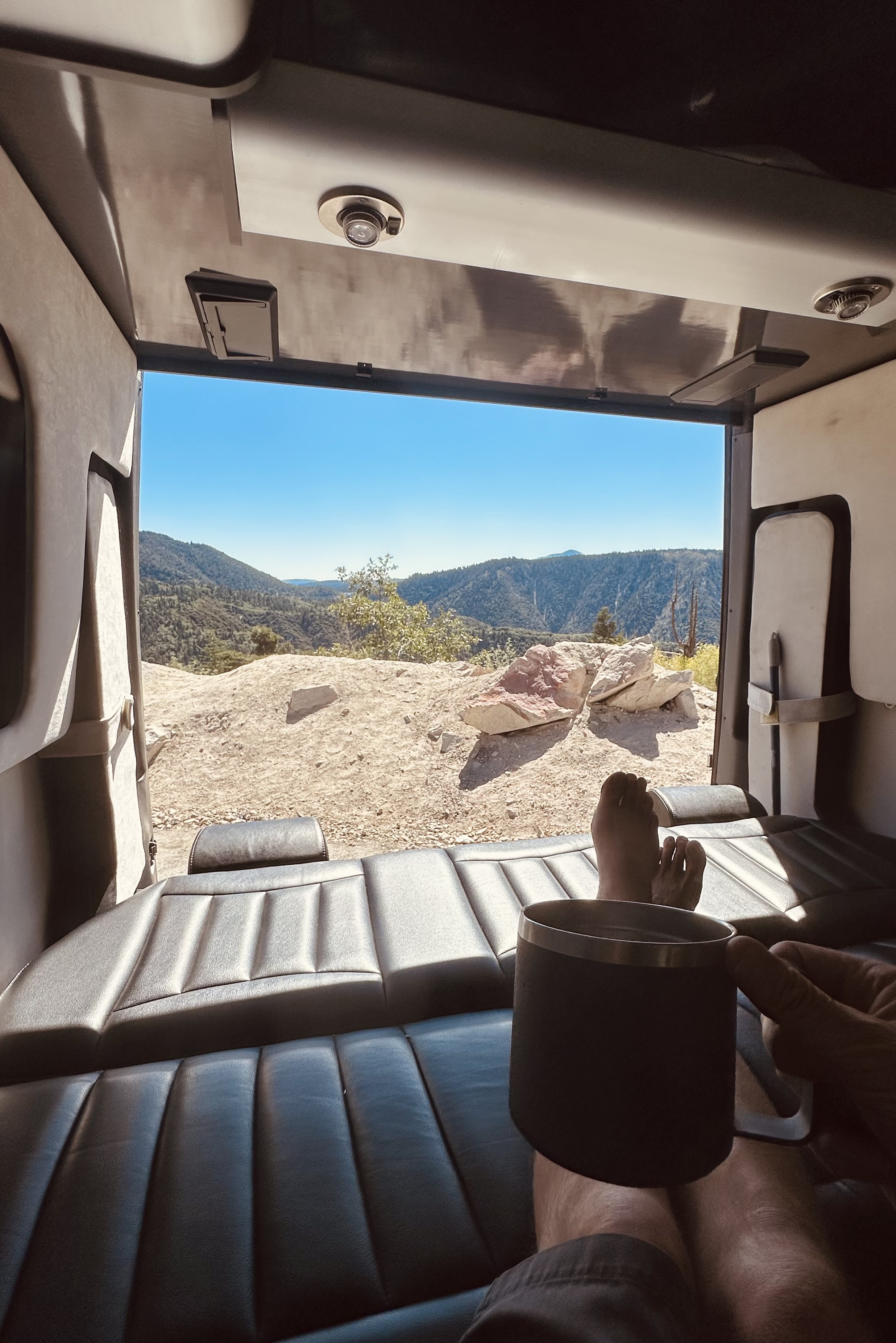 Inside a spacious RV rental, a person enjoys coffee with feet up, looking out at panoramic mountain views.. Airstream Interstate 2016