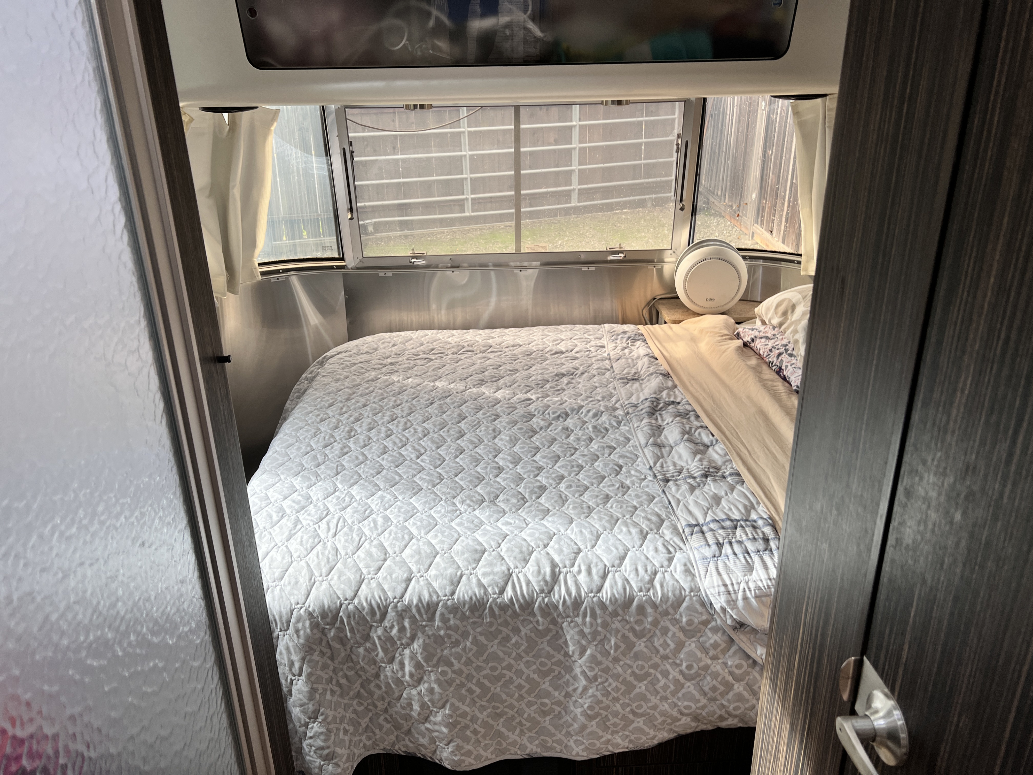 A glimpse into a comfortable rv rental bedroom featuring a large bed with a light patterned quilt and panoramic windows.. Airstream International 2017