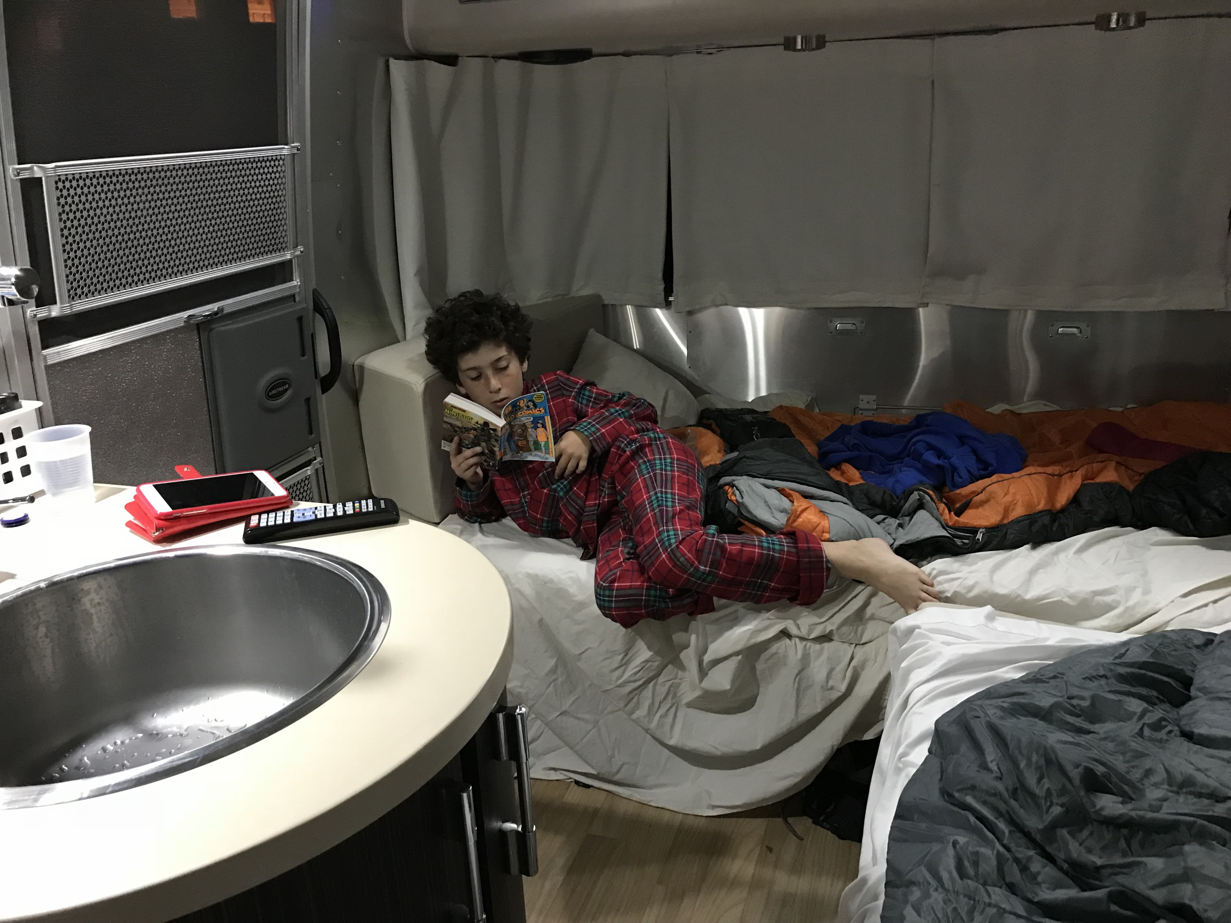 A child in plaid pajamas reads comfortably on a bed in an RV rental, showing the cozy interior.. Airstream International 2017