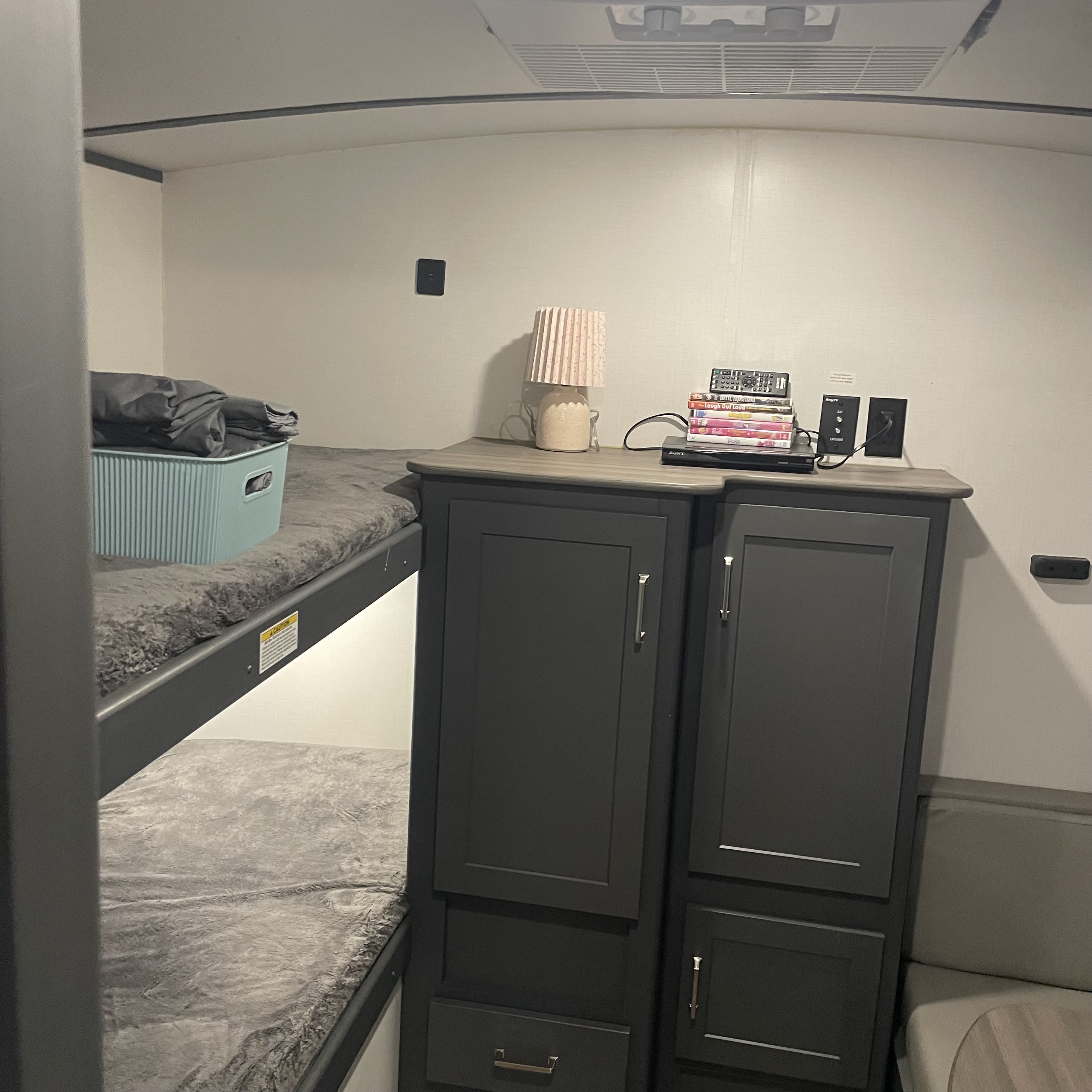 Inside an RV rental: cozy bunk beds with gray blankets, dark cabinets, a lamp, and entertainment setup.. Keystone RV Bullet Ultra Lite 2022