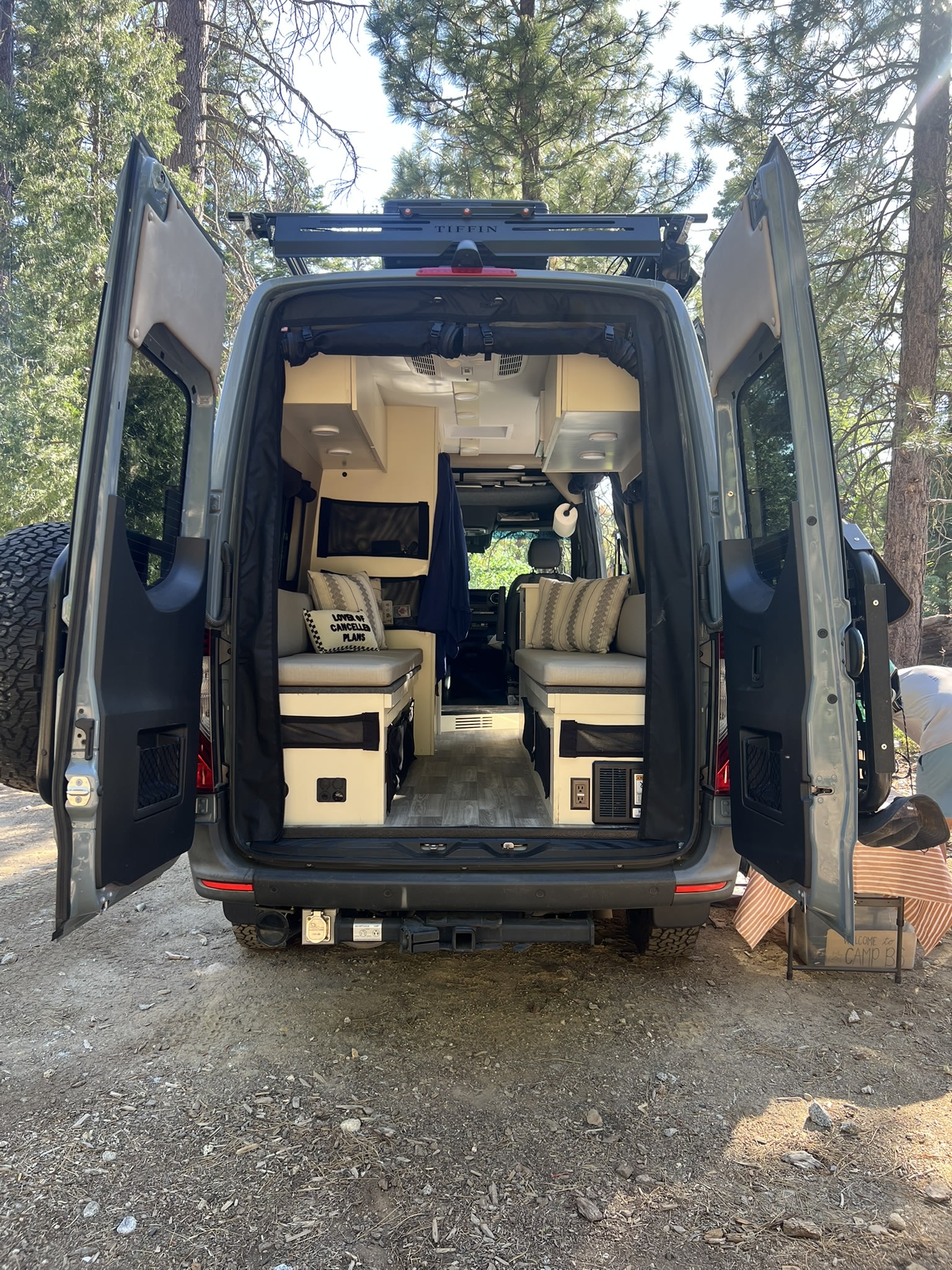 Spacious RV rental camper van interior with open doors, showcasing cozy seating/bed areas and storage in a peaceful forest setting.. Cahaba Cahaba Class B 2022
