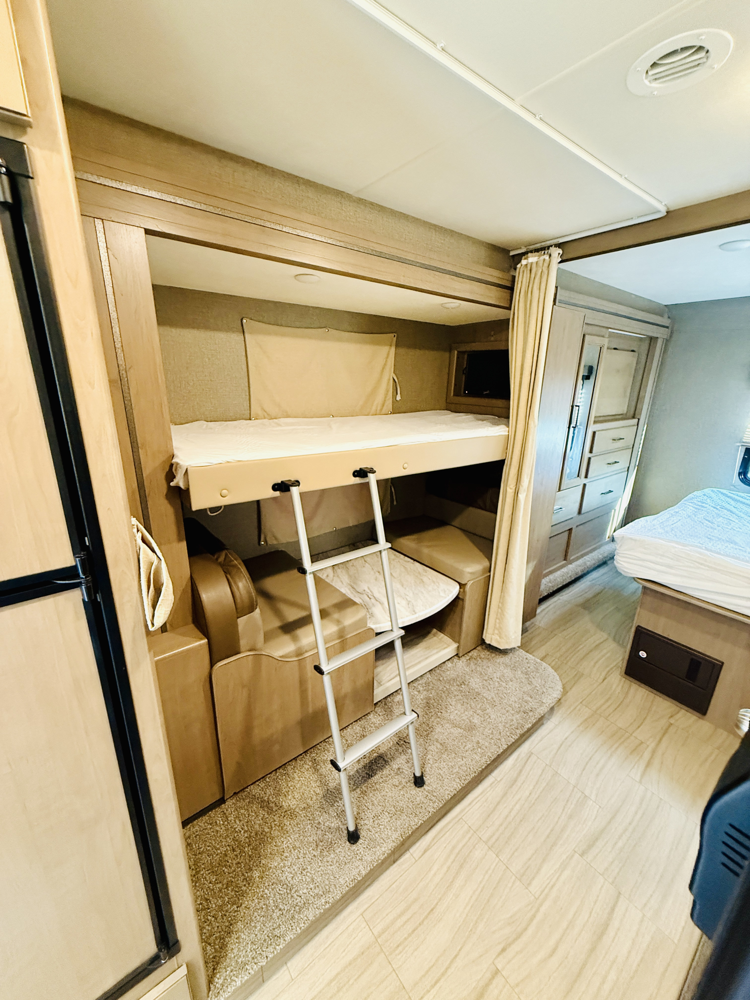 Inside an RV rental: cozy bunk beds with ladder, compact dinette, and main bed, optimized for family comfort.. Thor Coleman 2021