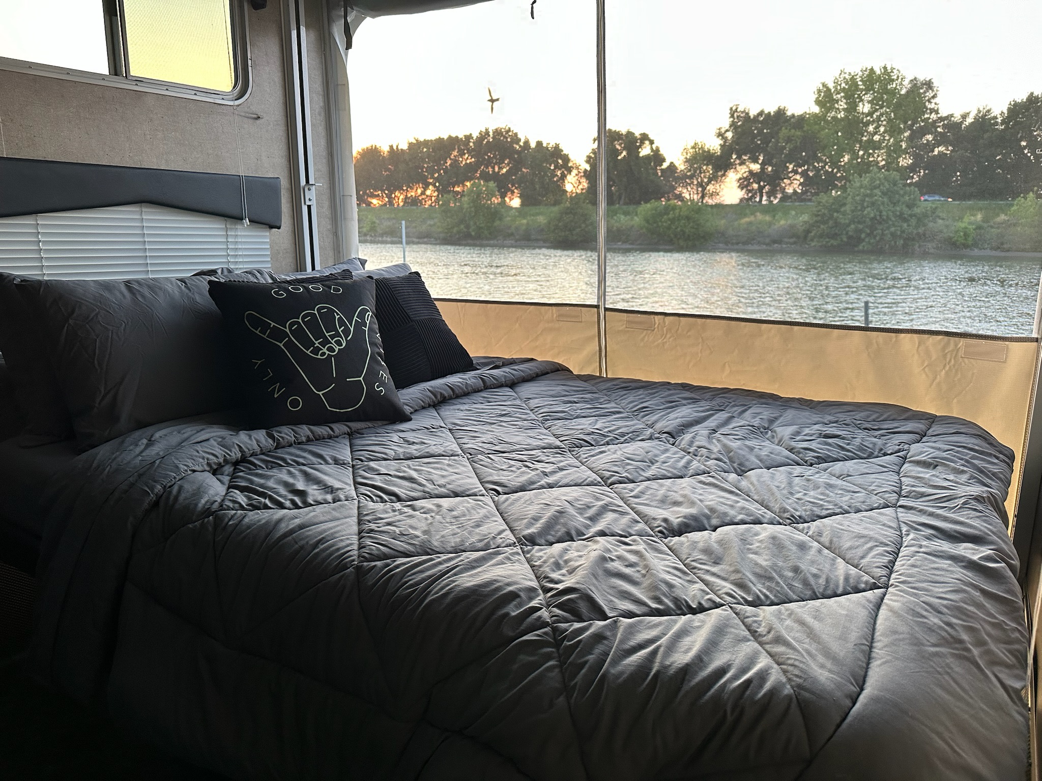 RV rental: Cozy bedroom with grey bedding & a 'GOOD VIBES ONLY' pillow, offering tranquil river views at sunset.. Forest River Sandstorm 2012