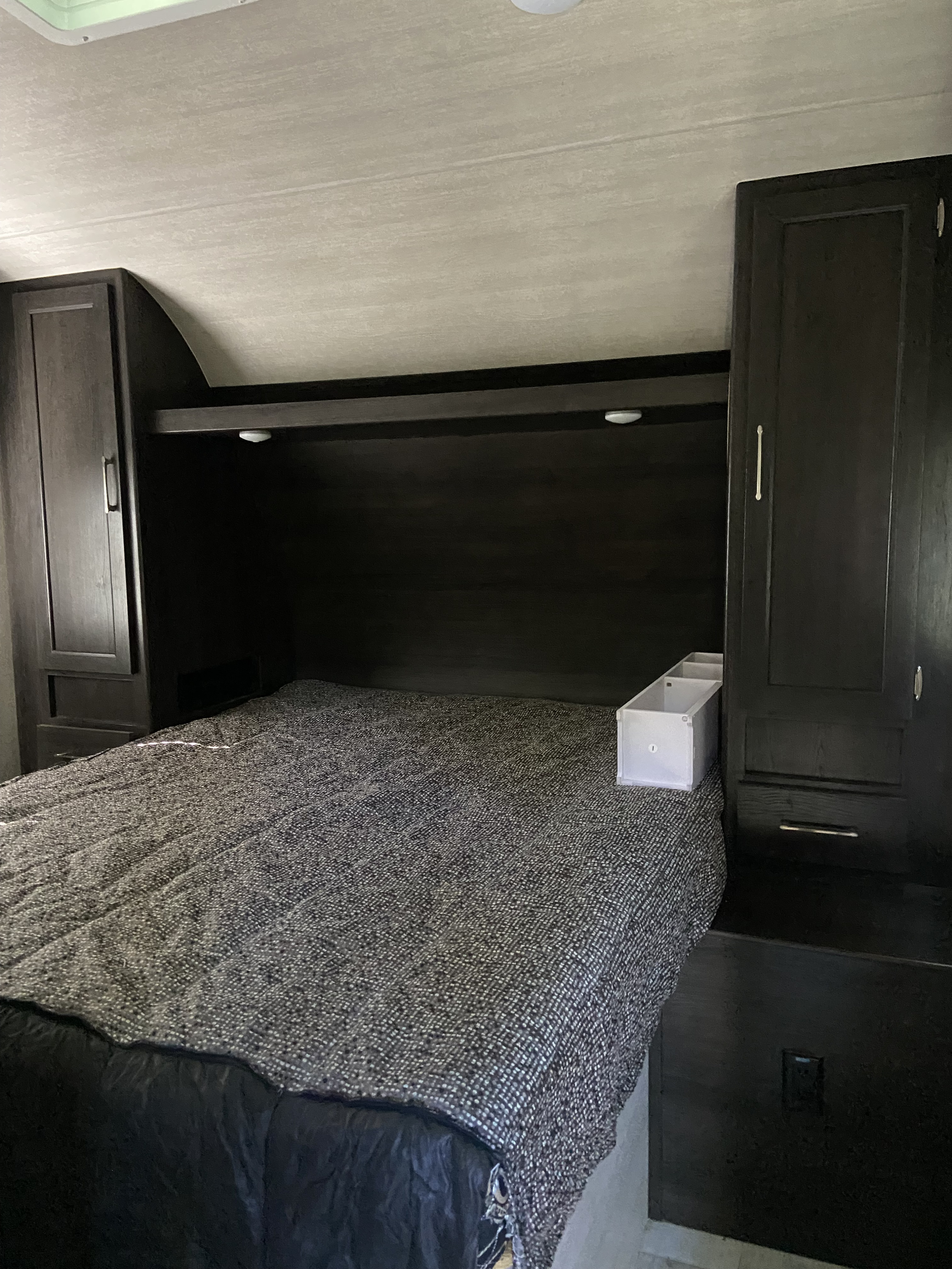 Cozy RV rental bedroom with a comfy bed, dark wood cabinets, and overhead storage, offering a functional sleeping area.. Genesis Supreme Rv Genesis Supreme 2022