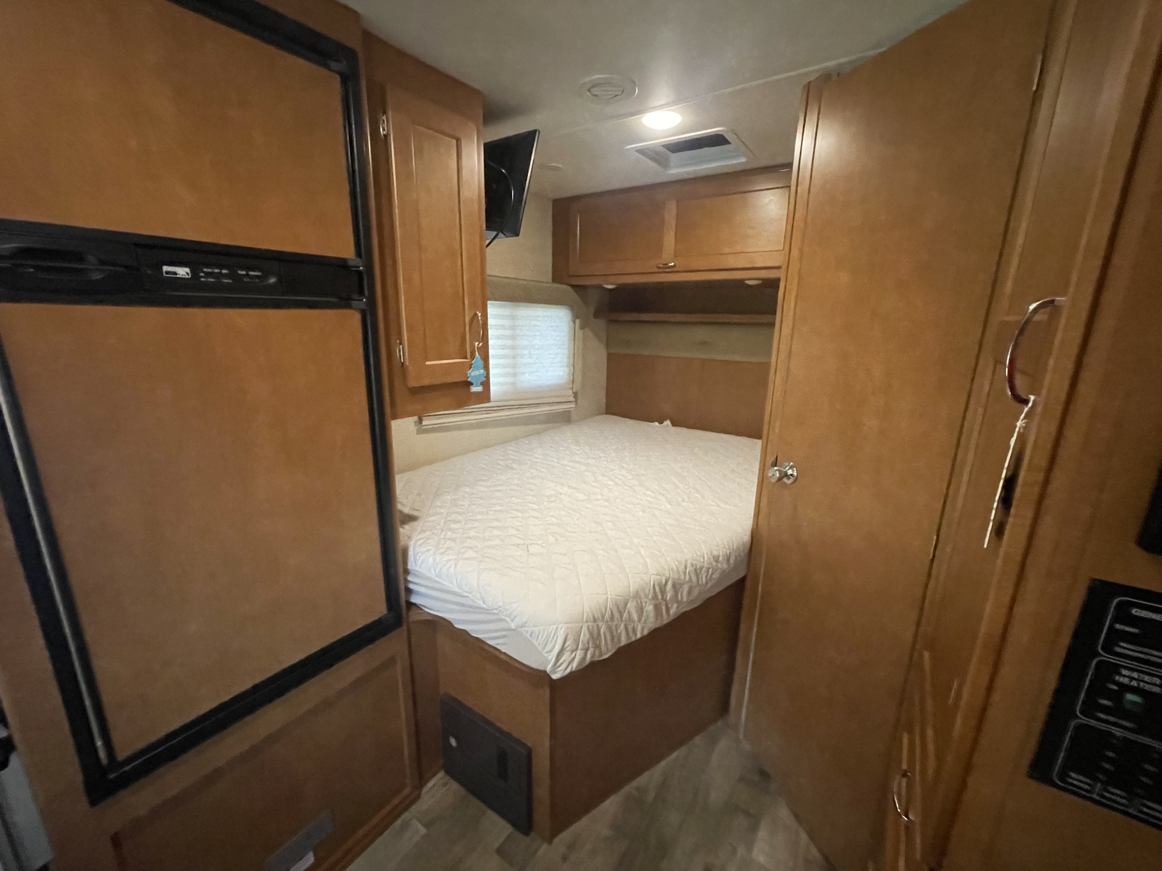 Compact RV rental bedroom with comfortable bed, fridge, wall-mounted TV, and overhead storage for a cozy stay.. Winnebago Minnie Winnie 2016
