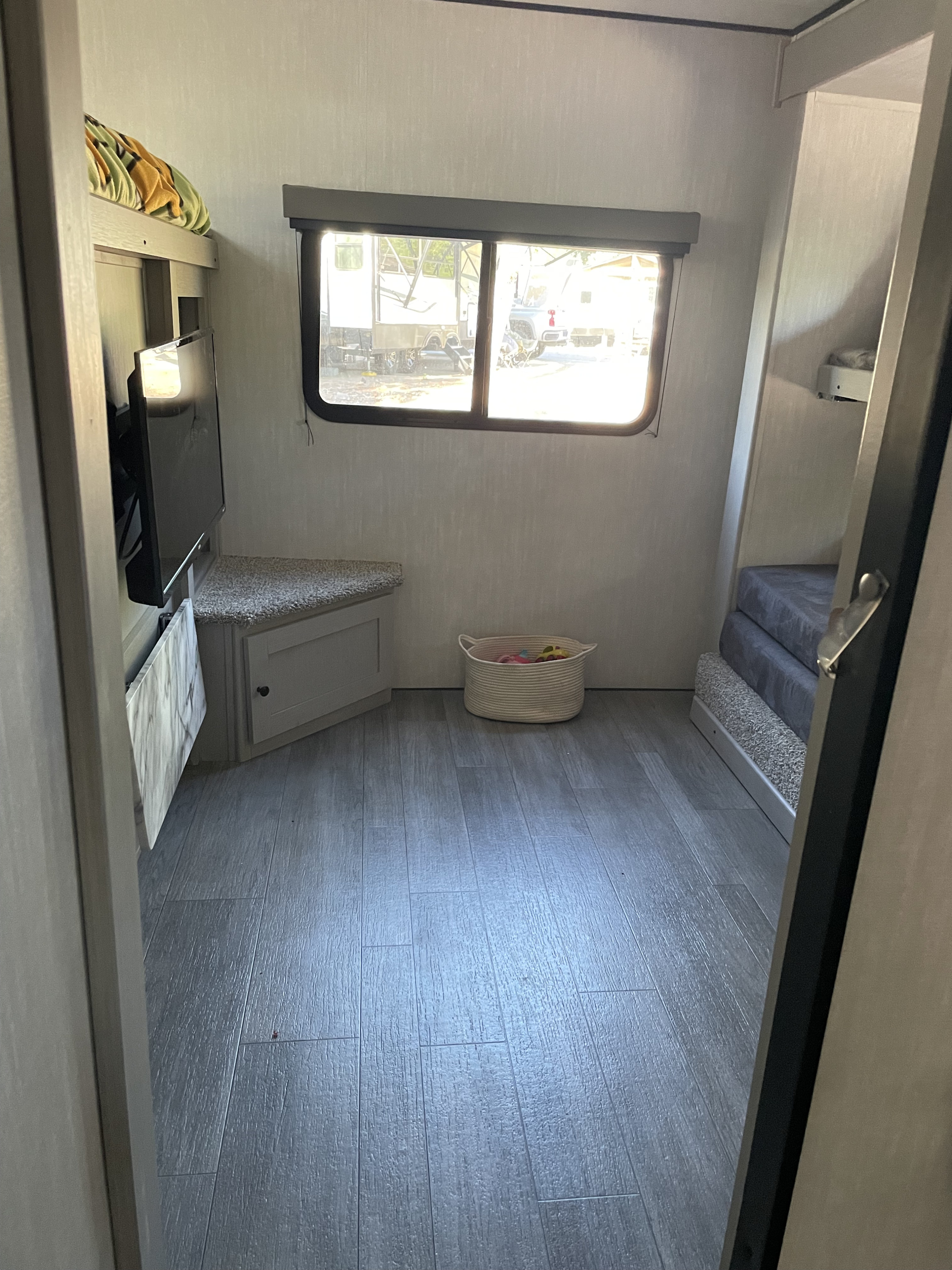 Bright RV rental bunk room with built-in bunk beds, mounted TV, storage bench, and toy basket on wood-look floor.. Coachmen Apex 300 BHS 2025