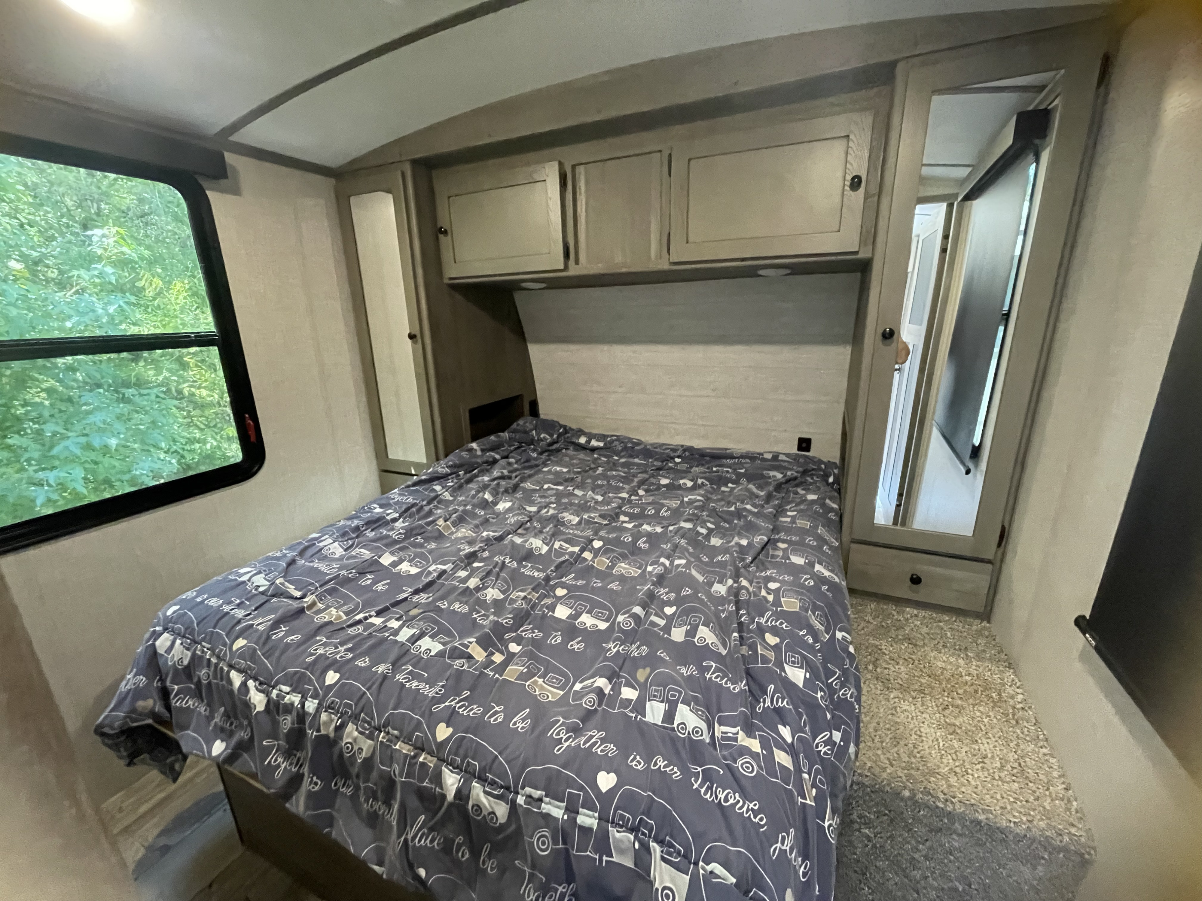 Cozy RV bedroom interior for your RV rental, with a bed, overhead storage, and natural light from the side window.. Keystone RV Outback 2020