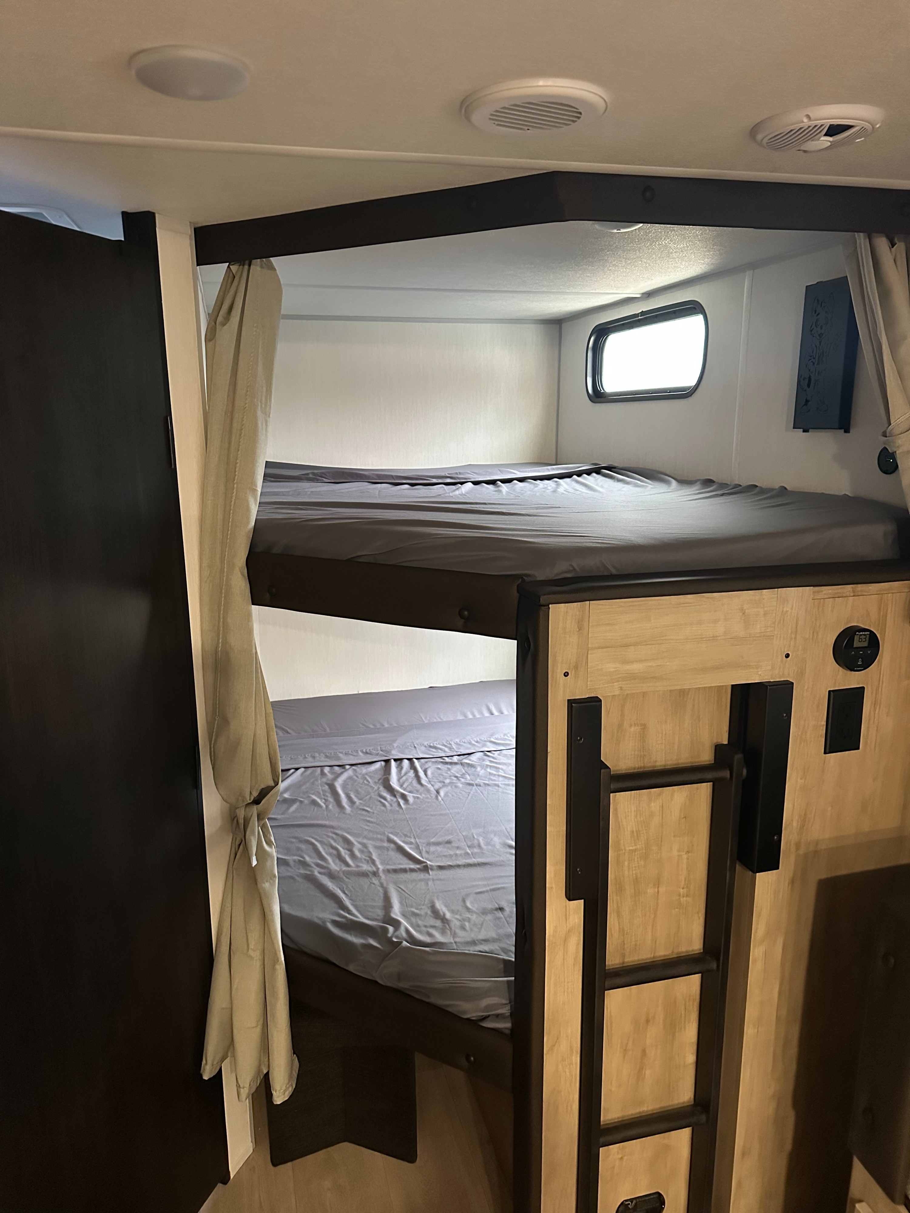 RV rental interior: two clean bunk beds with grey sheets, a ladder, and overhead vents visible.. Forest River Cherokee Grey Wolf 2026