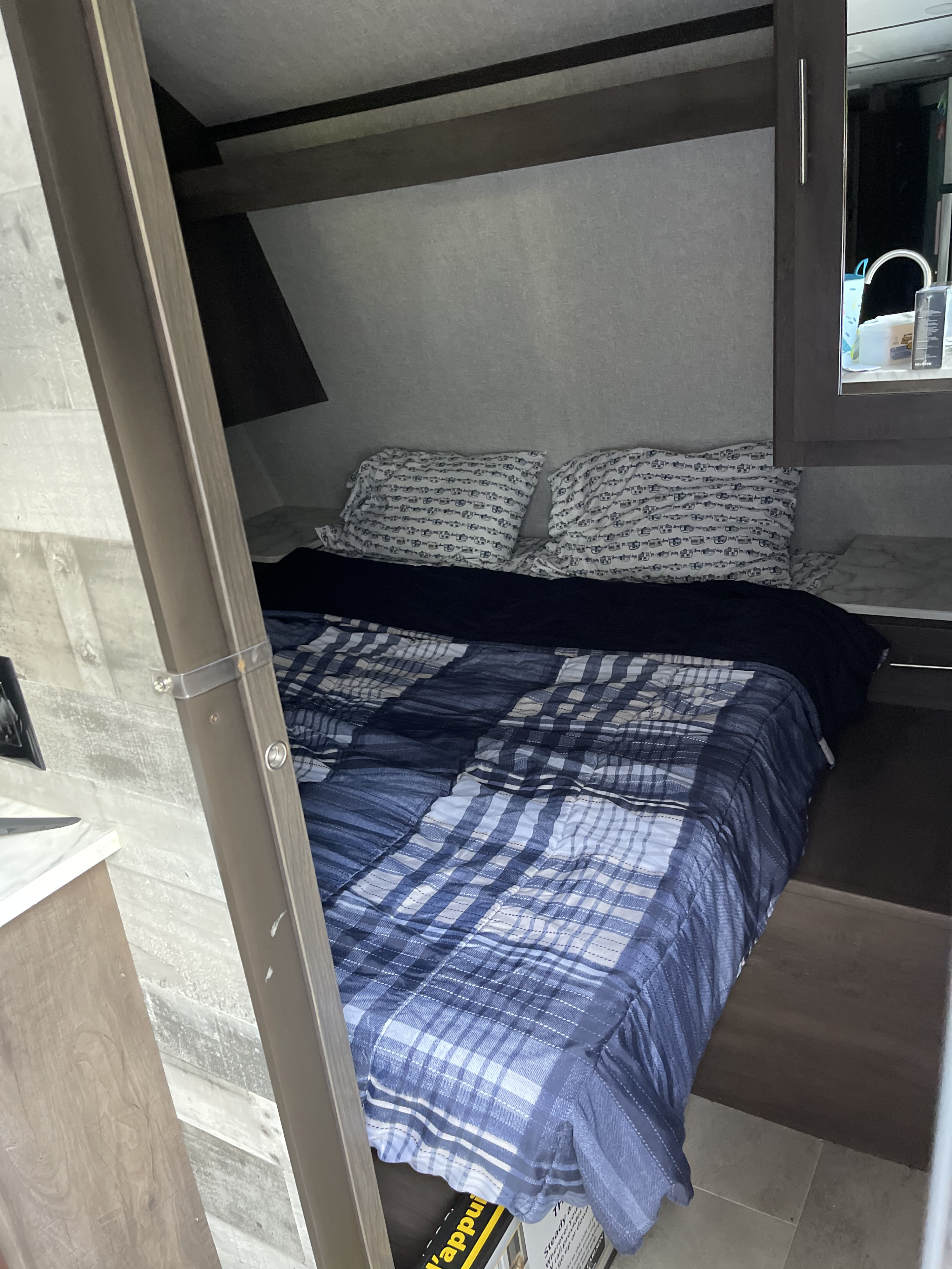 Cozy RV rental bedroom with plaid bedding and compact storage, perfect for your next adventure.. Dutchmen Coleman Lantern 2021