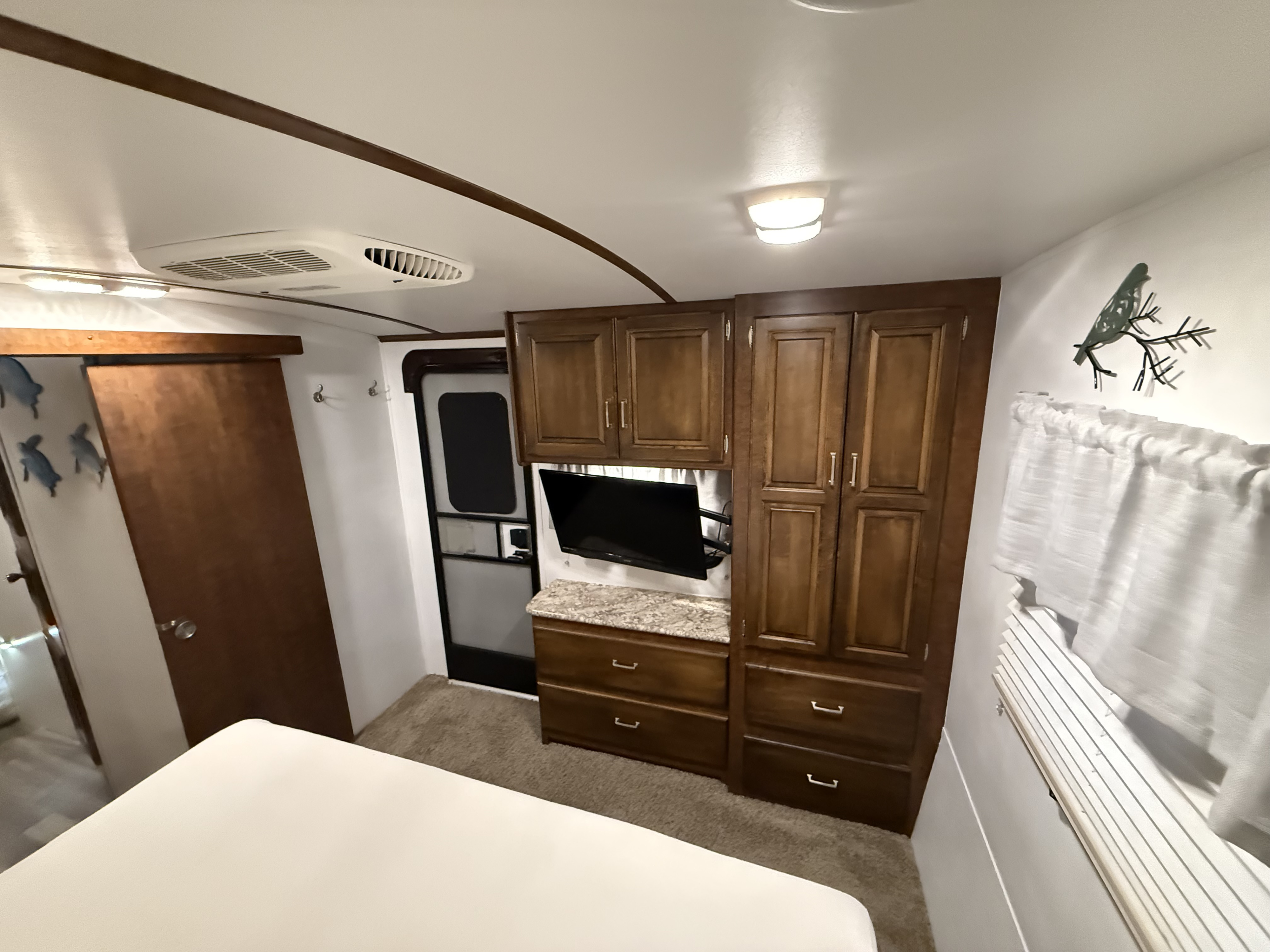 Inside this RV rental bedroom, find rich wood cabinets, a wall-mounted TV, AC, and a comfy bed. Optimized for travel.. Keystone Outback 2017