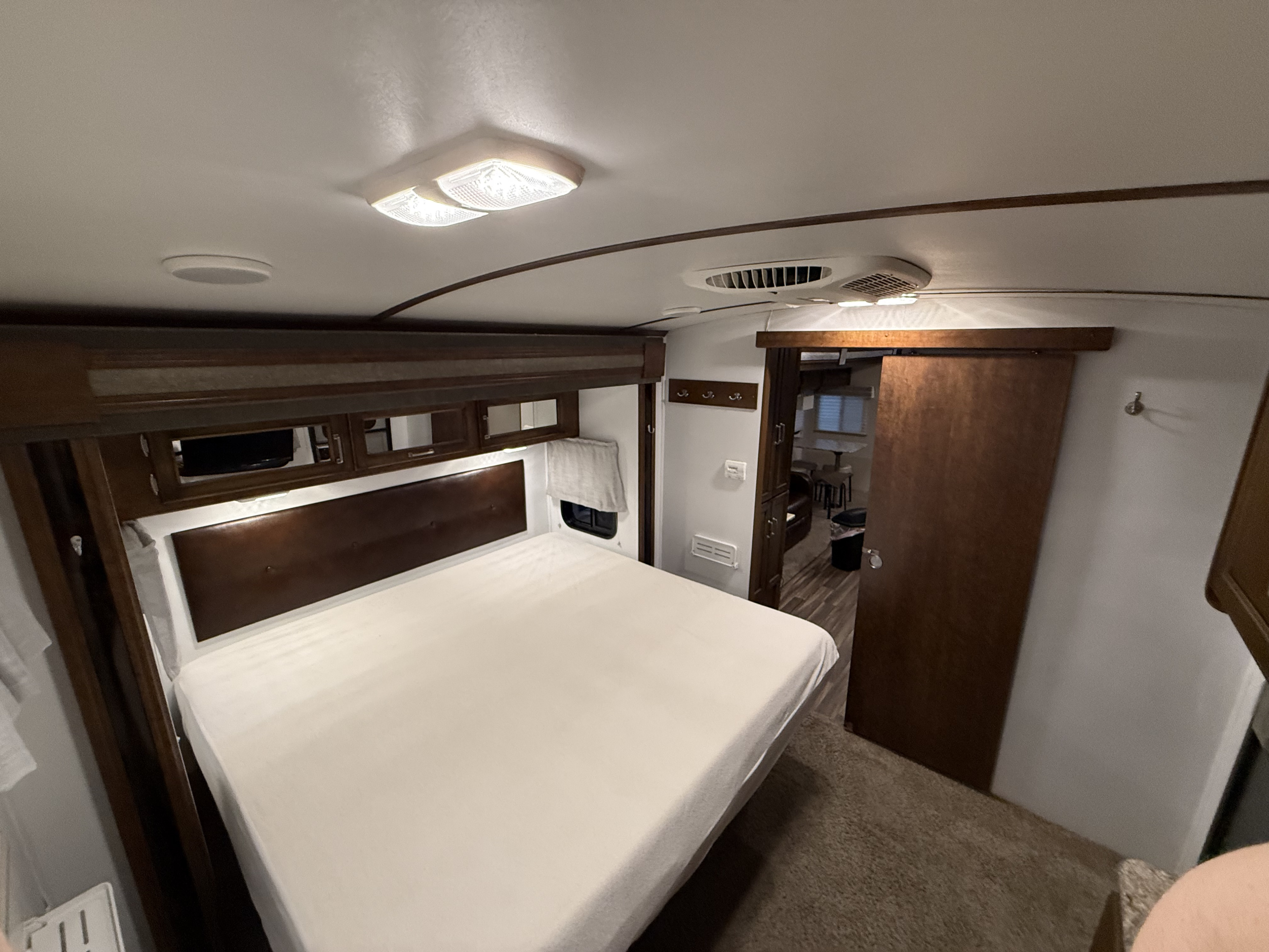 Inside an RV rental, a cozy bedroom featuring a queen bed, dark wood accents, and a sliding door to the main living space.. Keystone Outback 2017