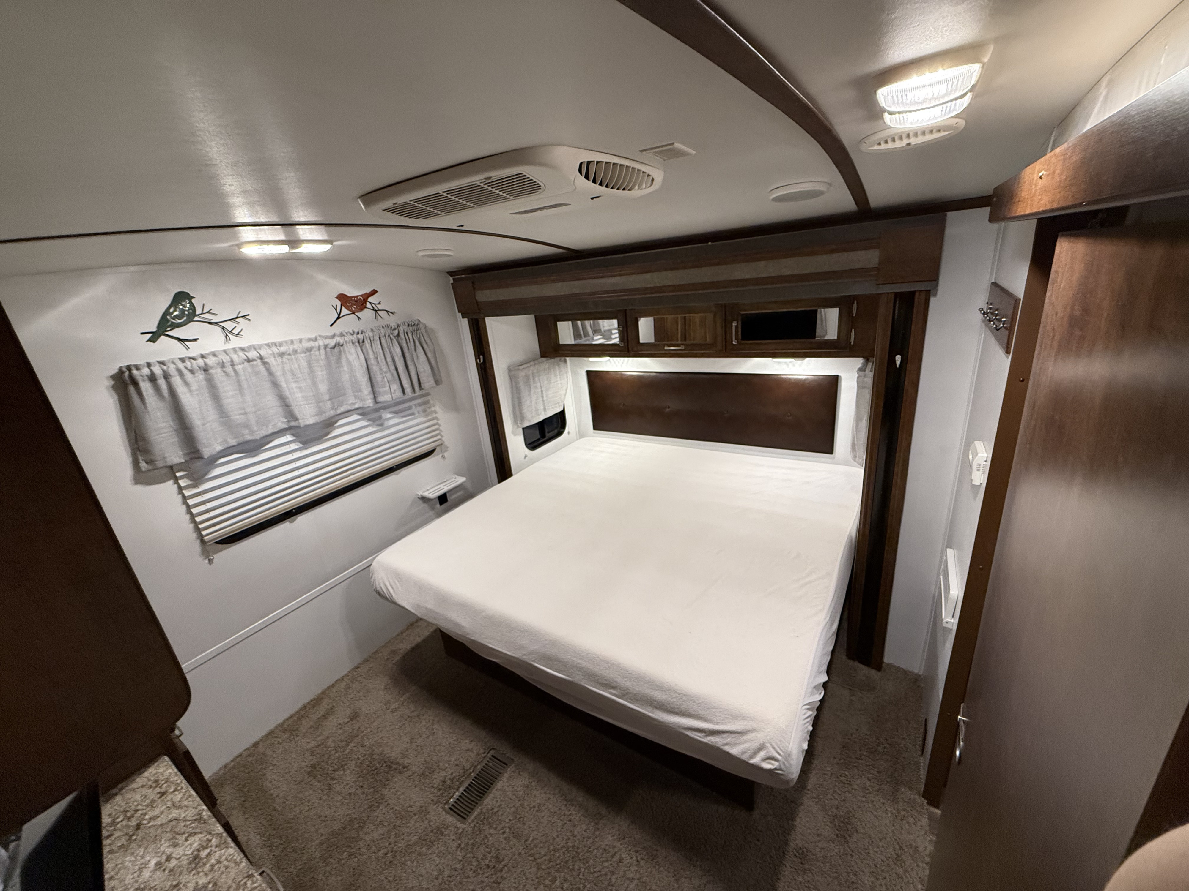 Cozy RV rental bedroom: A comfortable bed, overhead cabinets, window blinds, and bird decor, with an AC unit and recessed lighting.. Keystone Outback 2017