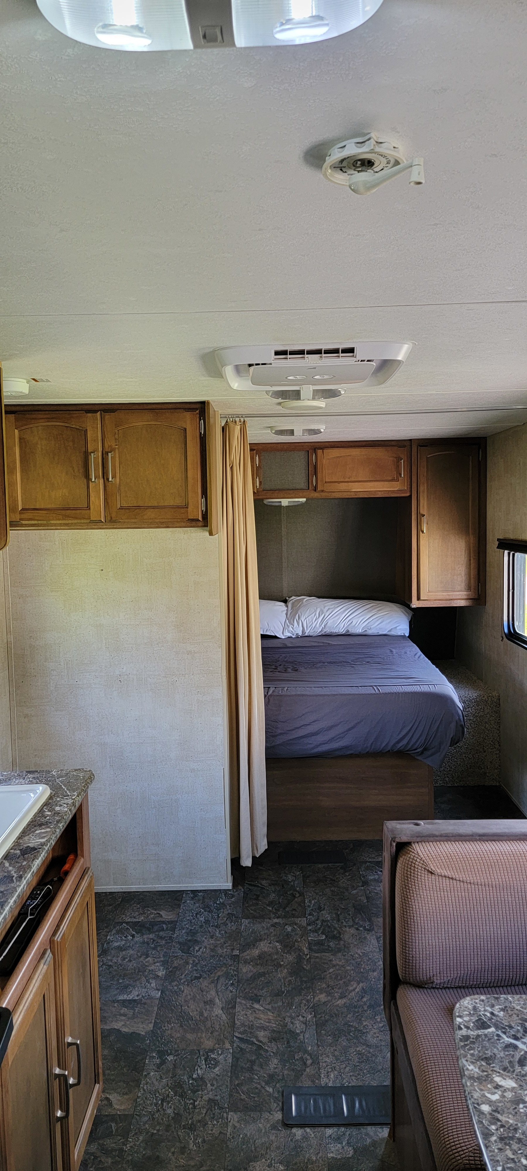 Interior of an RV rental: a bed with privacy curtain, kitchen counter, and dining booth. Overhead AC unit and lights.. Keystone RV Summerland 2015