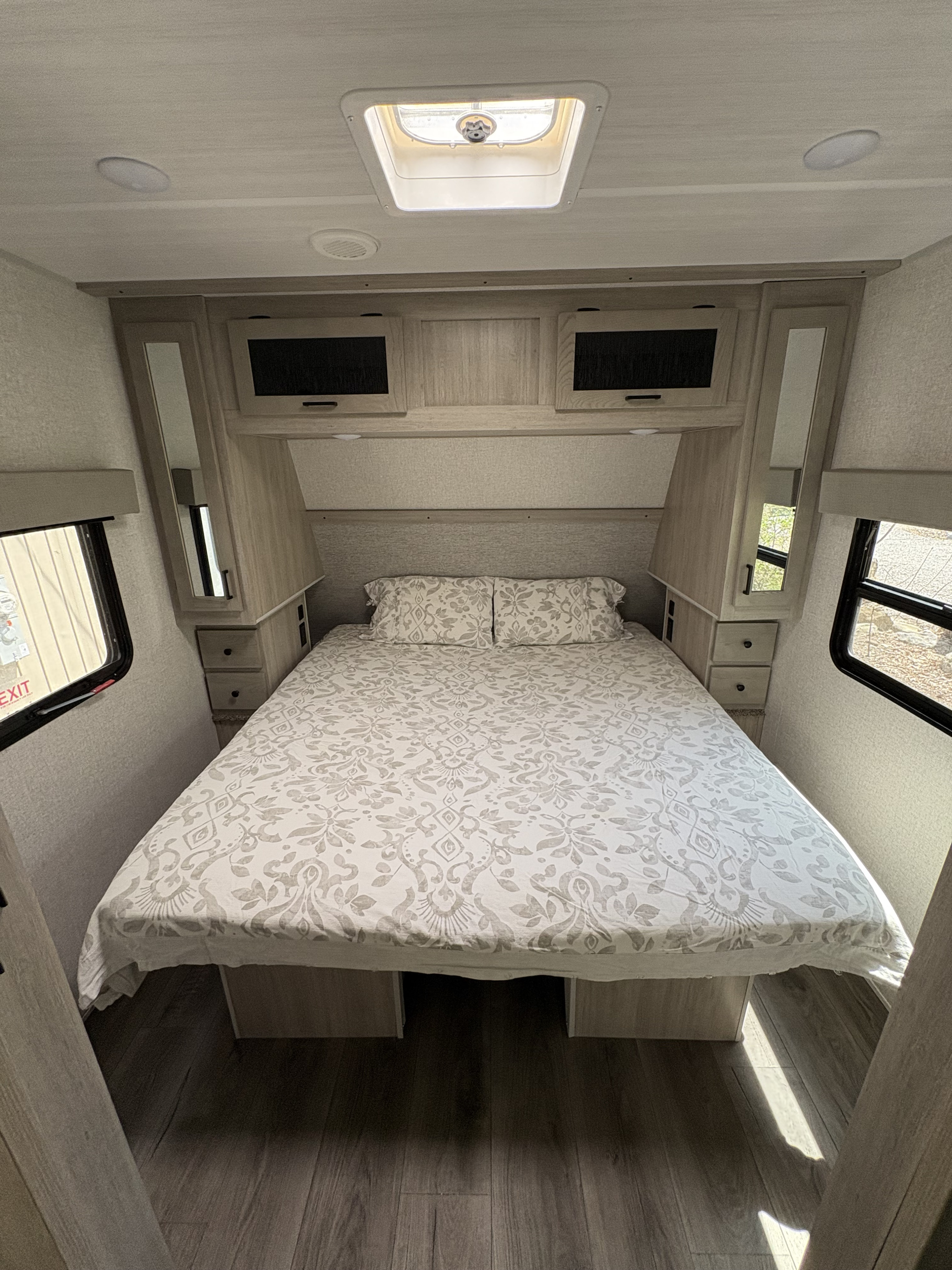 This cozy RV rental bedroom features a patterned bed, built-in storage, side windows, and a skylight for comfortable travel.. East to West Alta 2022