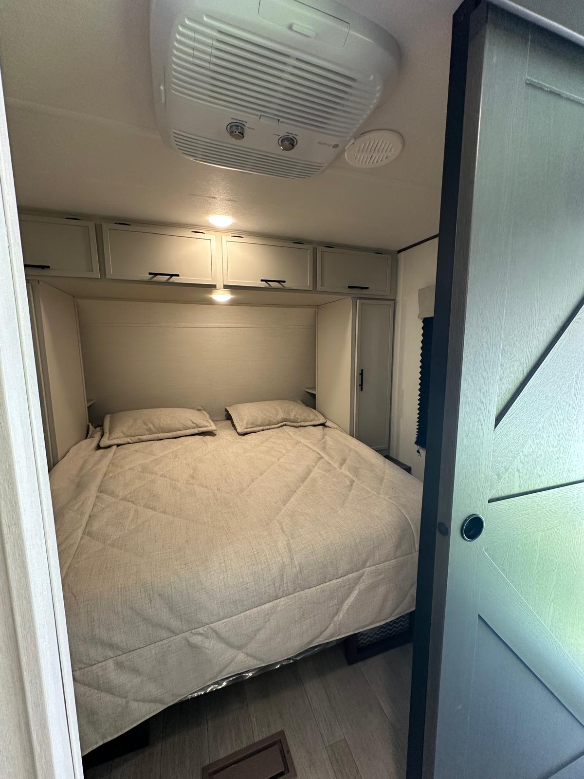 Inside an RV rental: a compact bedroom featuring a comfortable bed, overhead storage, and ceiling-mounted AC.. Prime Time Avenger 2026