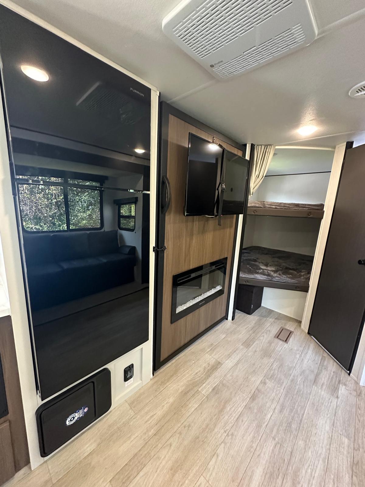 RV rental interior with a Furrion fridge, TV, electric fireplace, bunk beds, and sofa reflection.. Prime Time Avenger 2026