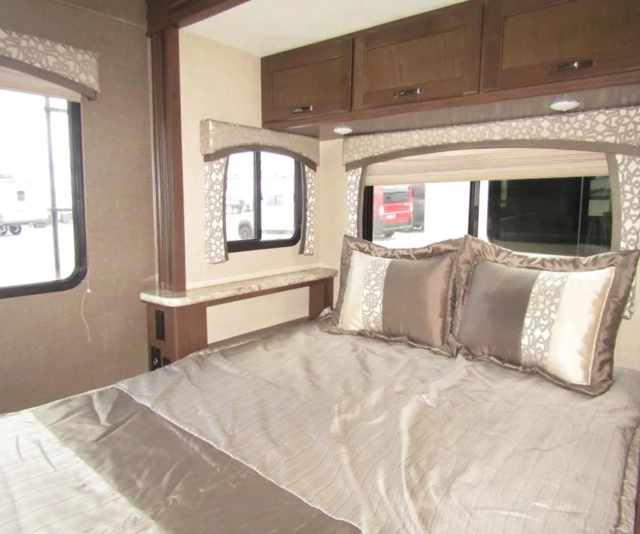 RV rental interior: a comfy bedroom featuring a bed with decorative pillows, ample overhead cabinets, and bright windows.. Thor Chateau 2019