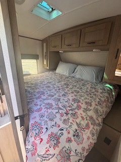 Comfortable RV rental bedroom with floral bedding, pillows, overhead cabinets, window, and a bright ceiling skylight.. Cruiser RV Shadow Cruiser 2021