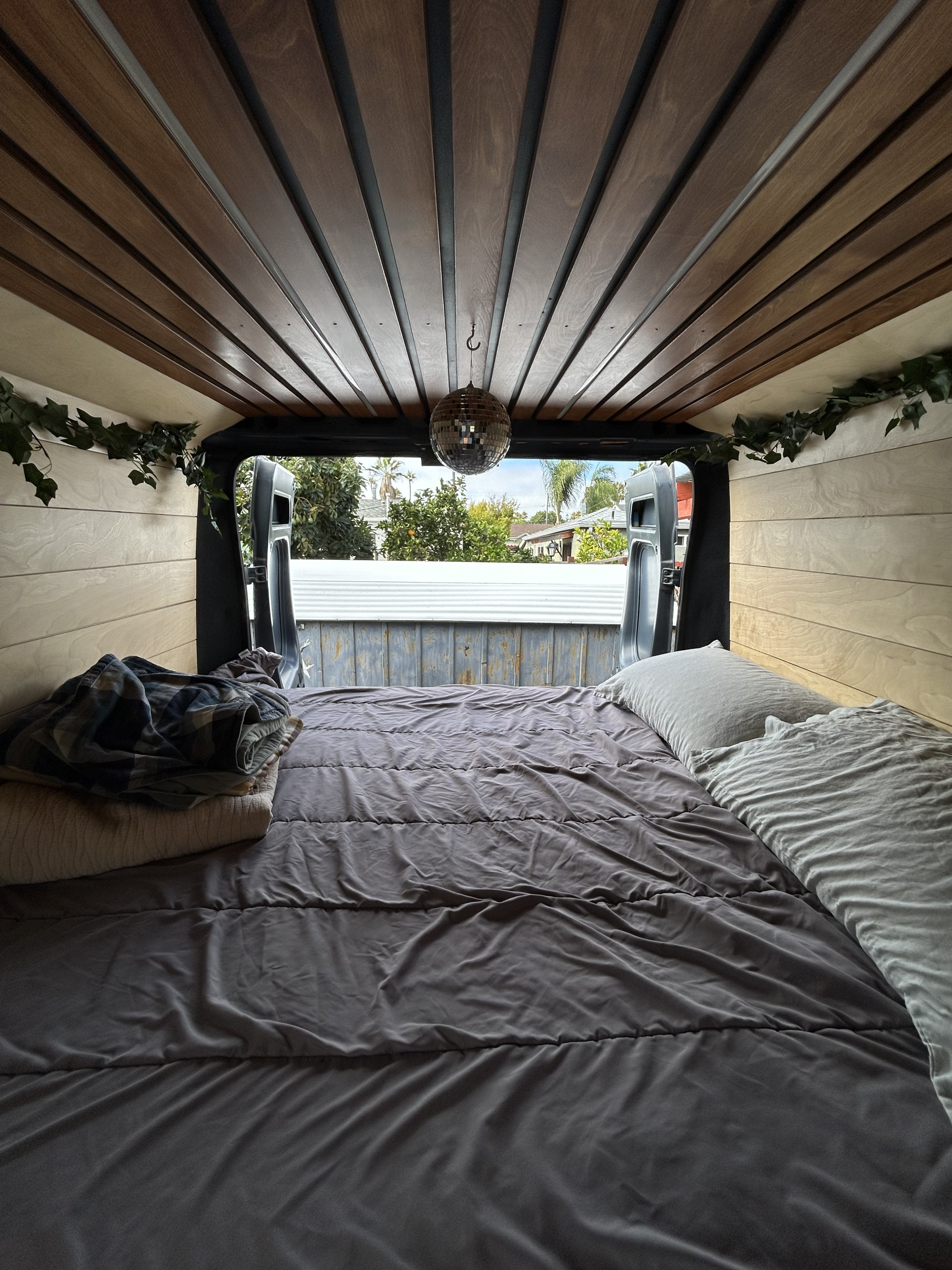 Cozy RV rental bedroom: wood interior, comfy bed, small disco ball, and outdoor view from open doors.. Dodge Ram Promaster 2500 2019