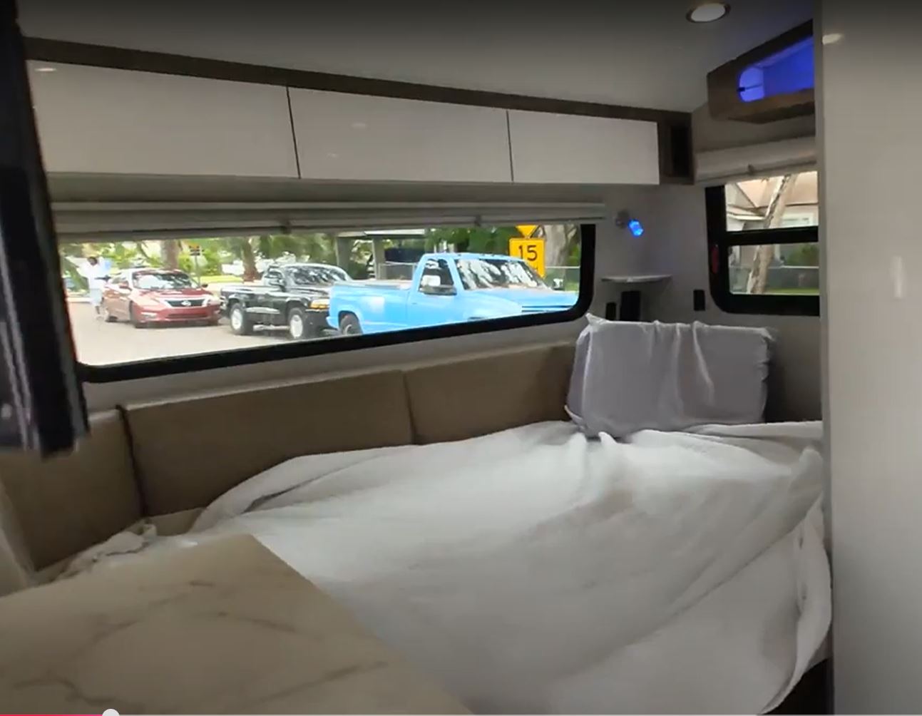 Inside an RV rental: a cozy bed/couch with white sheets, and a window view of a red car, black truck, and blue truck outside.. InTech RV InTech RV Trailer 2020