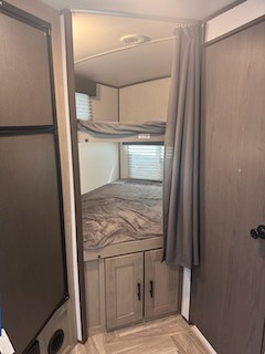 Interior view of an RV rental showing two bunk beds with dark gray bedding and a storage cabinet, plus a privacy curtain.. Cruiser RV Shadow Cruiser 2021
