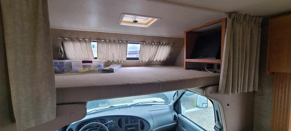 RV rental: Interior view of the over-cab bunk bed with windows, TV nook, ceiling vent, and driver's cabin below.. Thor Four Winds 2016