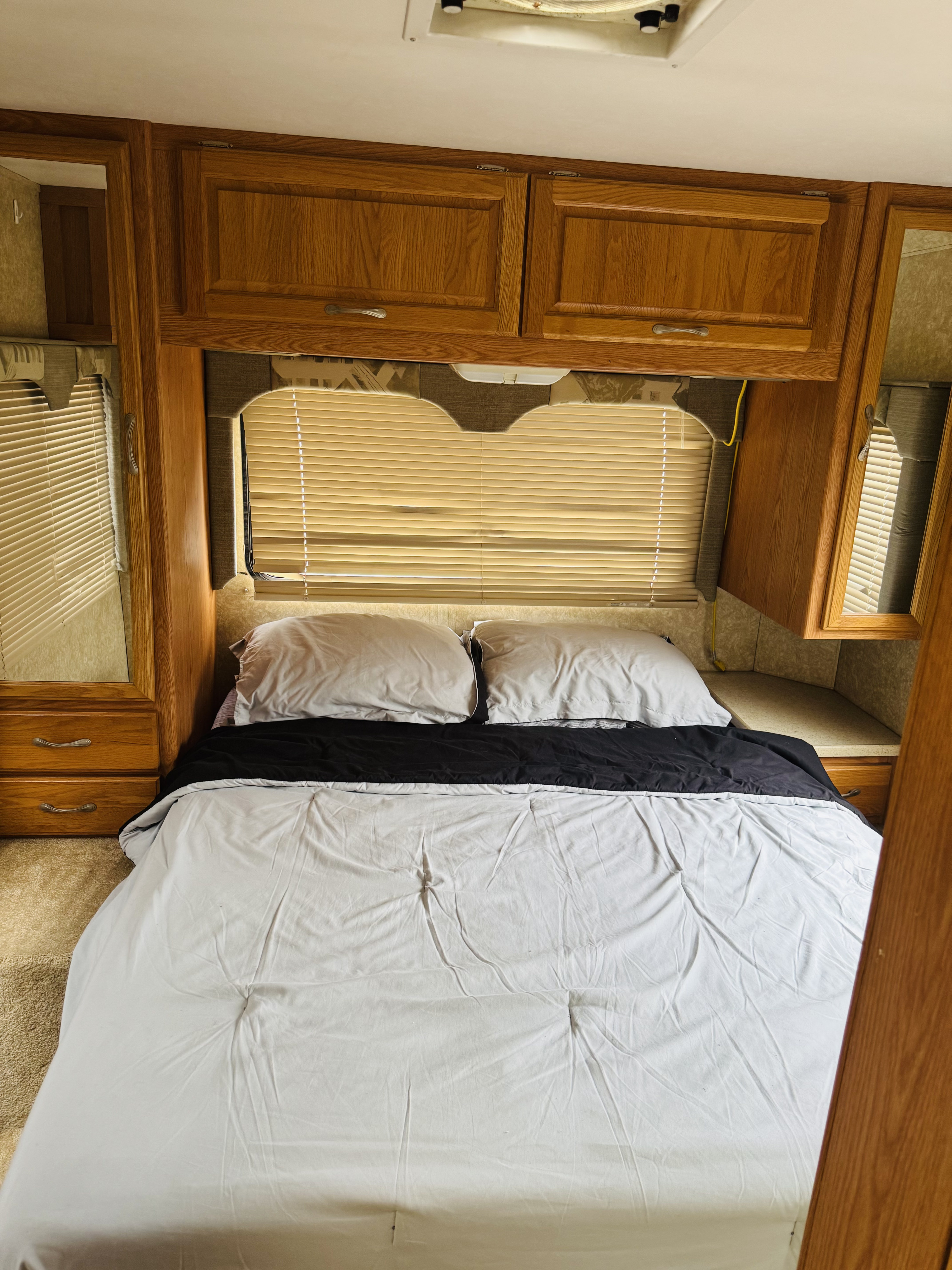 RV rental: Compact RV bedroom featuring a bed with grey pillows, black and white bedding, wooden cabinets, and window blinds.. Thor Four Winds 2016