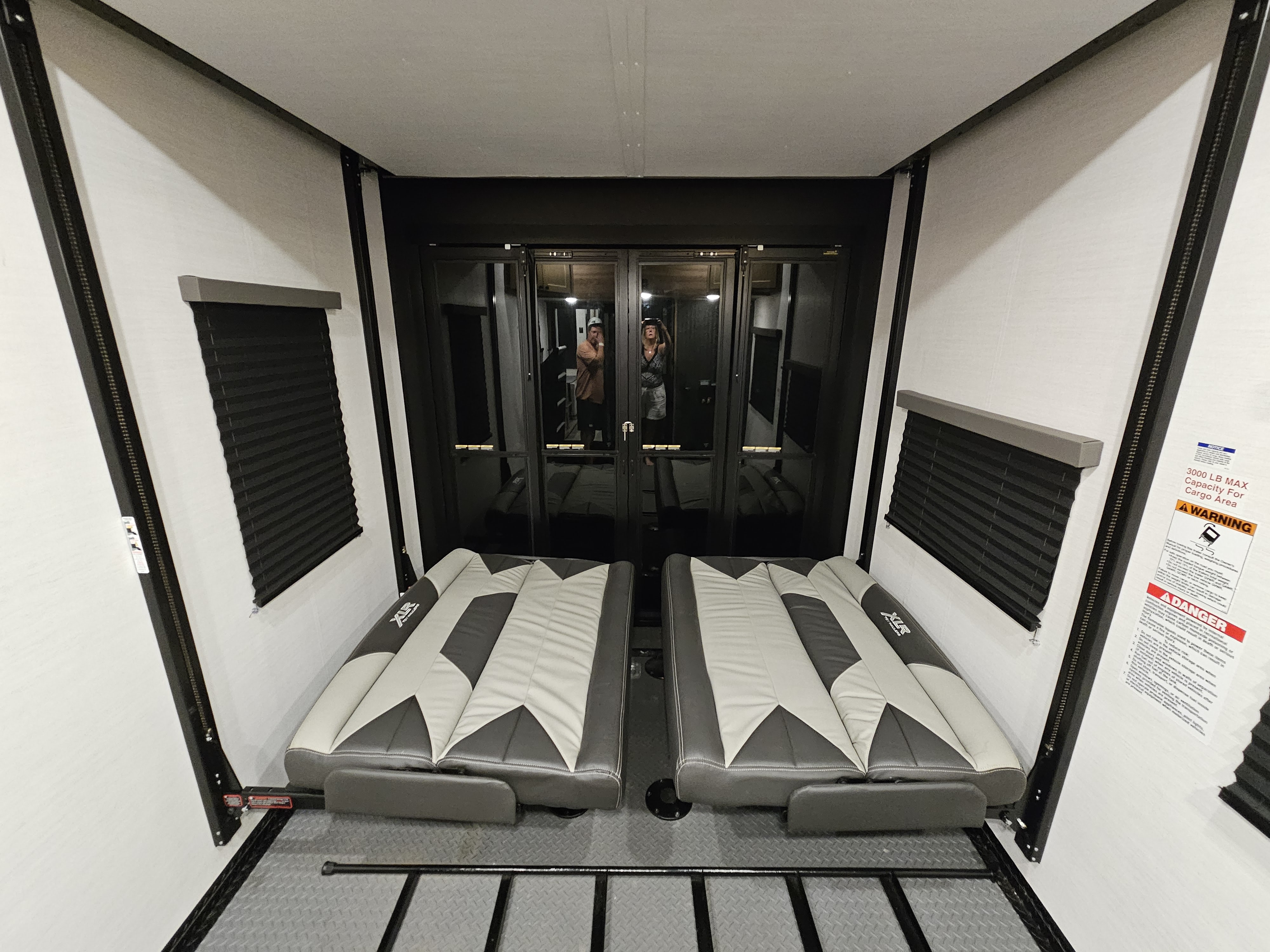 Spacious RV rental toy hauler's cargo area, equipped with two fold-down sofas and large reflective doors. Capacity warnings visible.. Forest River XLR Nitro 2023