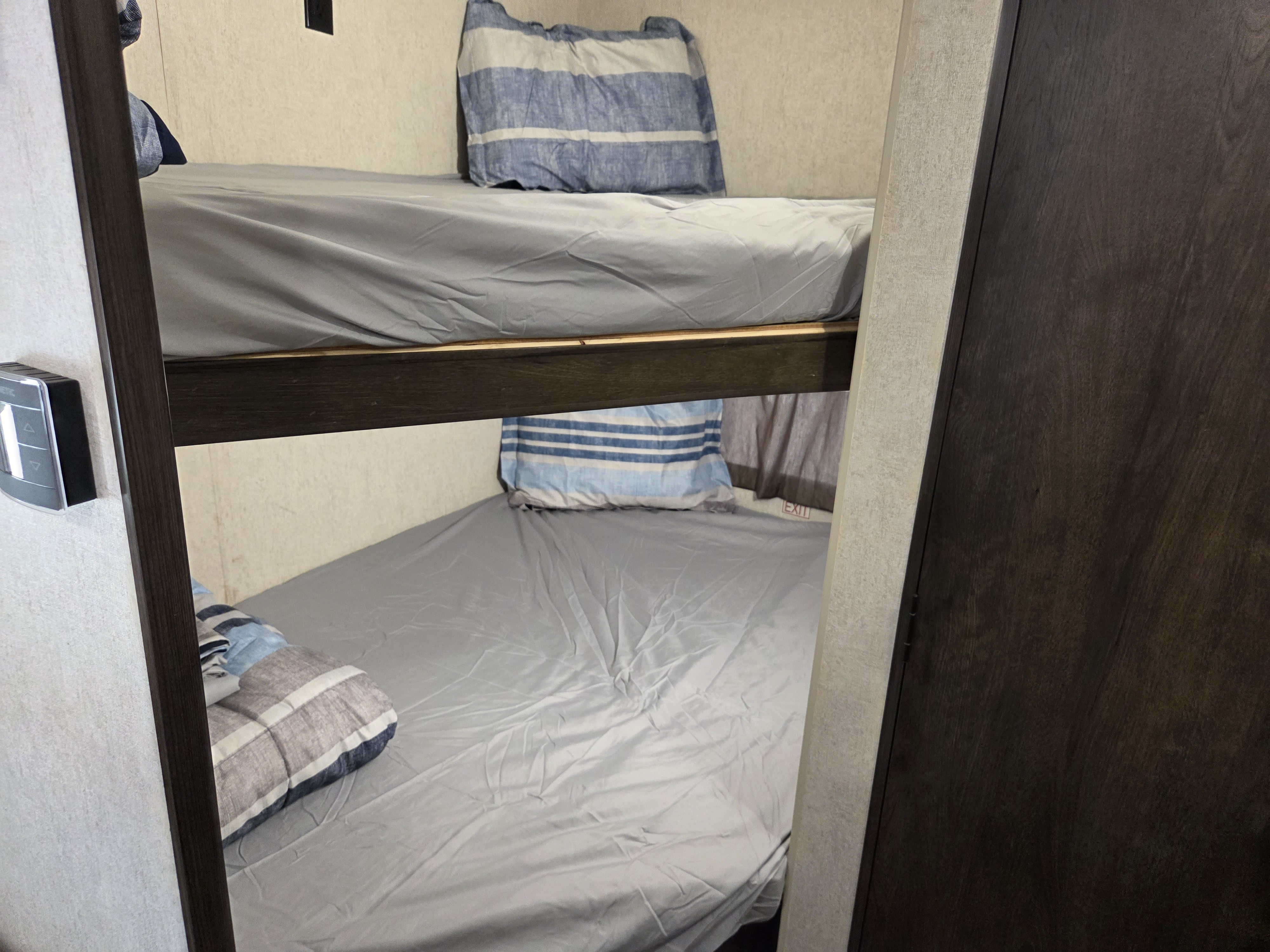 Inside an RV rental: view of two neatly made bunk beds with grey sheets & striped pillows. Compact sleeping area for adventure. Features thermostat on wall.. Starcraft Autumn Ridge Outfitter 2019