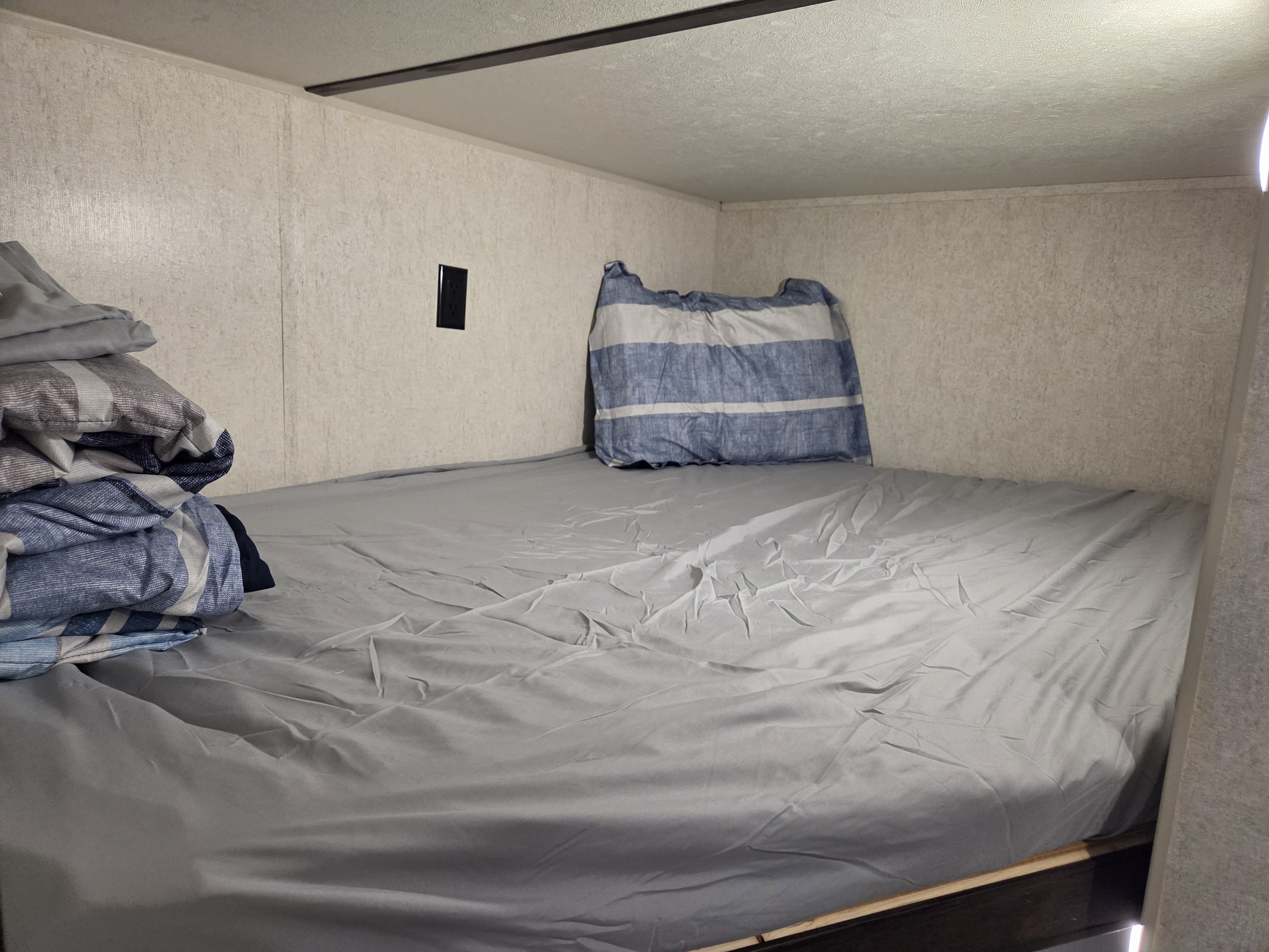 Cozy RV rental bunk bed with grey sheets and a blue striped pillow and folded blankets, ideal for compact travel.. Starcraft Autumn Ridge Outfitter 2019