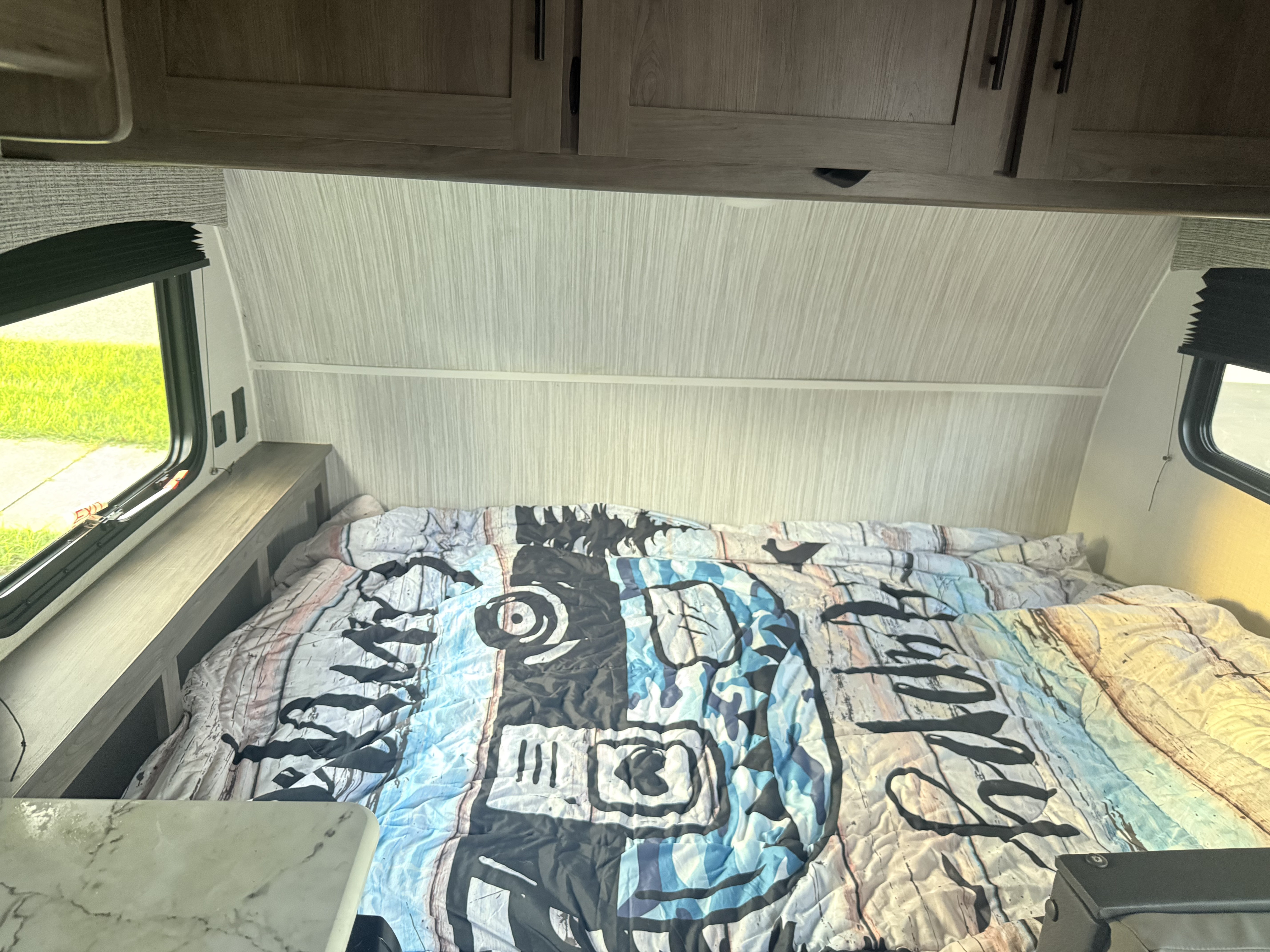 Cozy RV rental bedroom featuring a bed with a unique comforter, overhead cabinets, and windows on both sides.. Clipper Clipper 2025