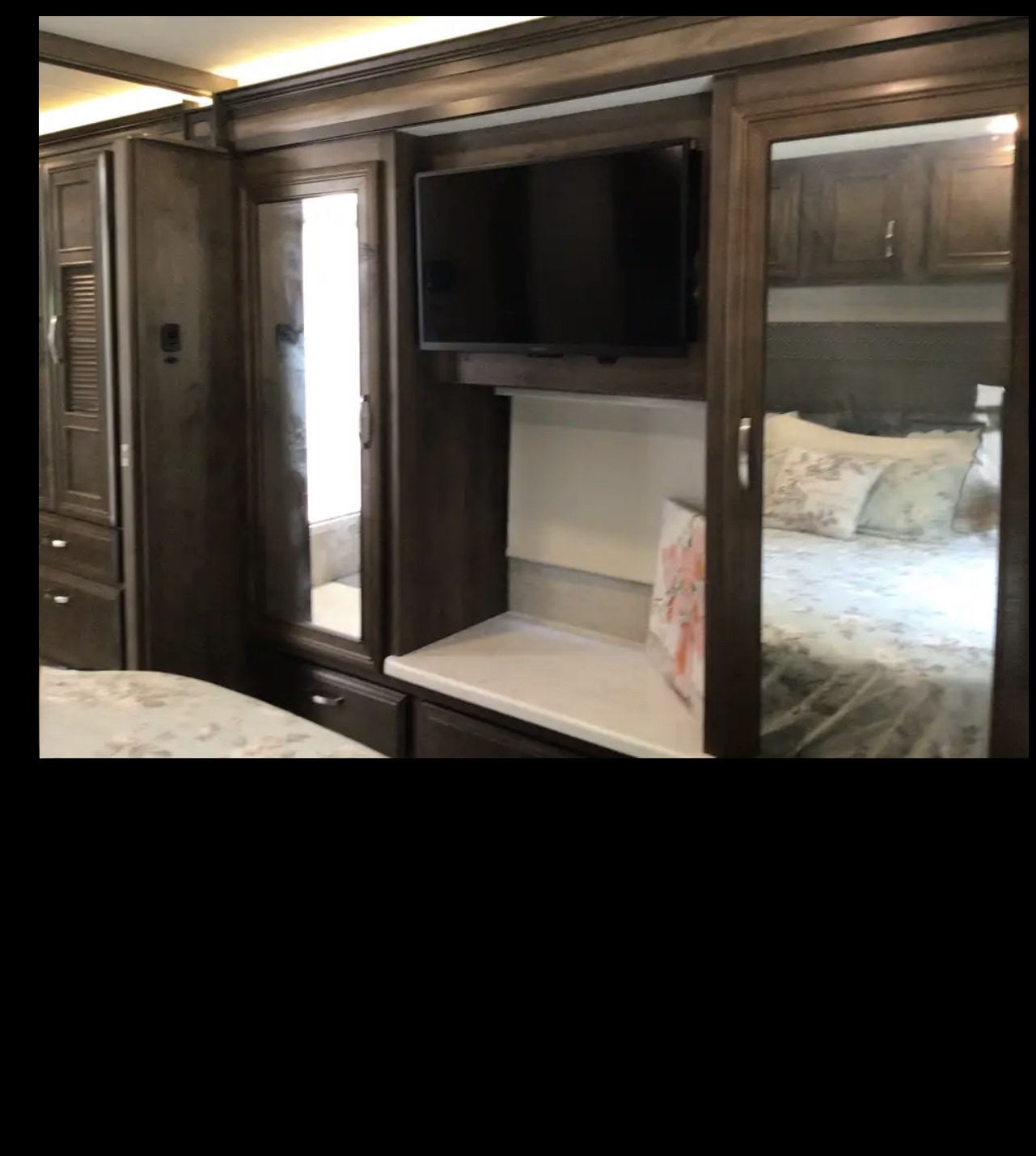 Modern RV rental bedroom interior: TV, mirrored closet door reflecting the bed, and dark wood storage cabinets.. Entegra Coach Vision XL 2022