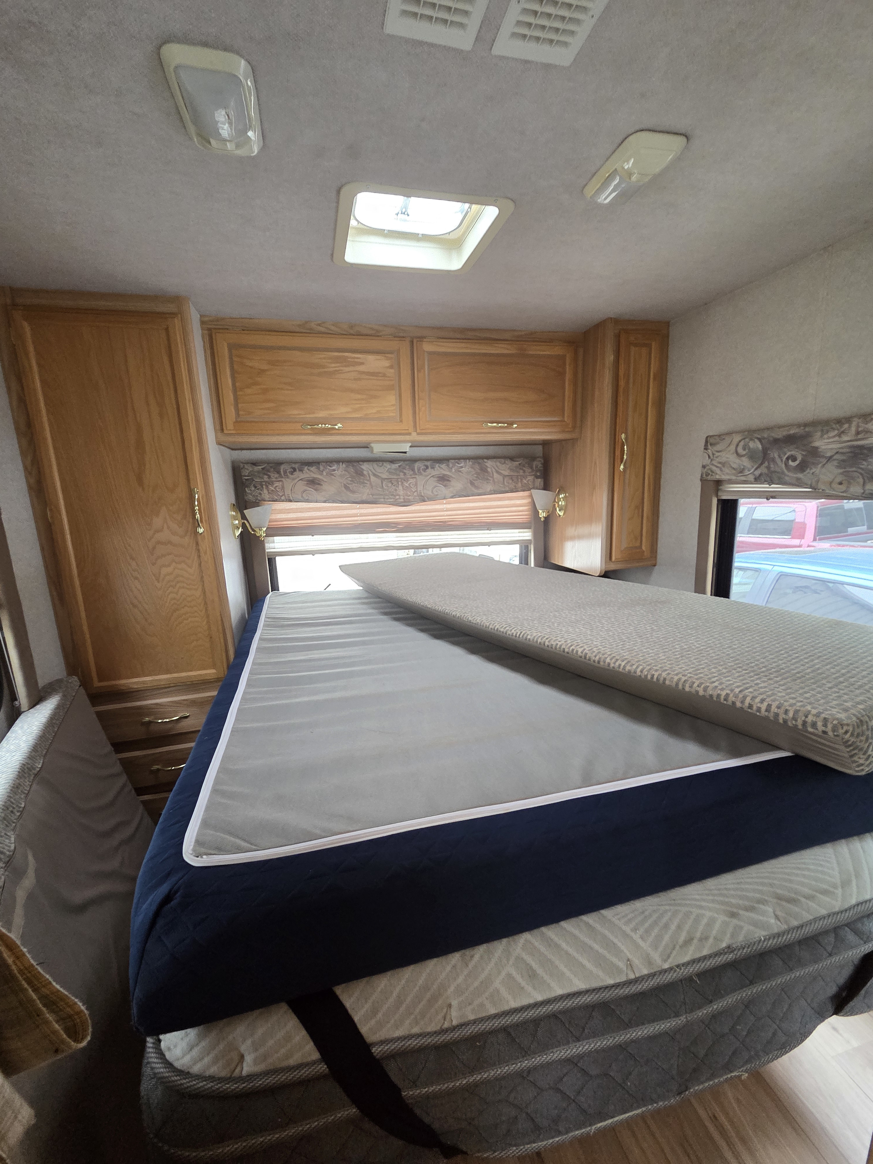 RV rental: a comfortable bedroom with layered mattresses, wooden cabinets, a window, and a skylight.. Tioga Tioga Motorhome 2001
