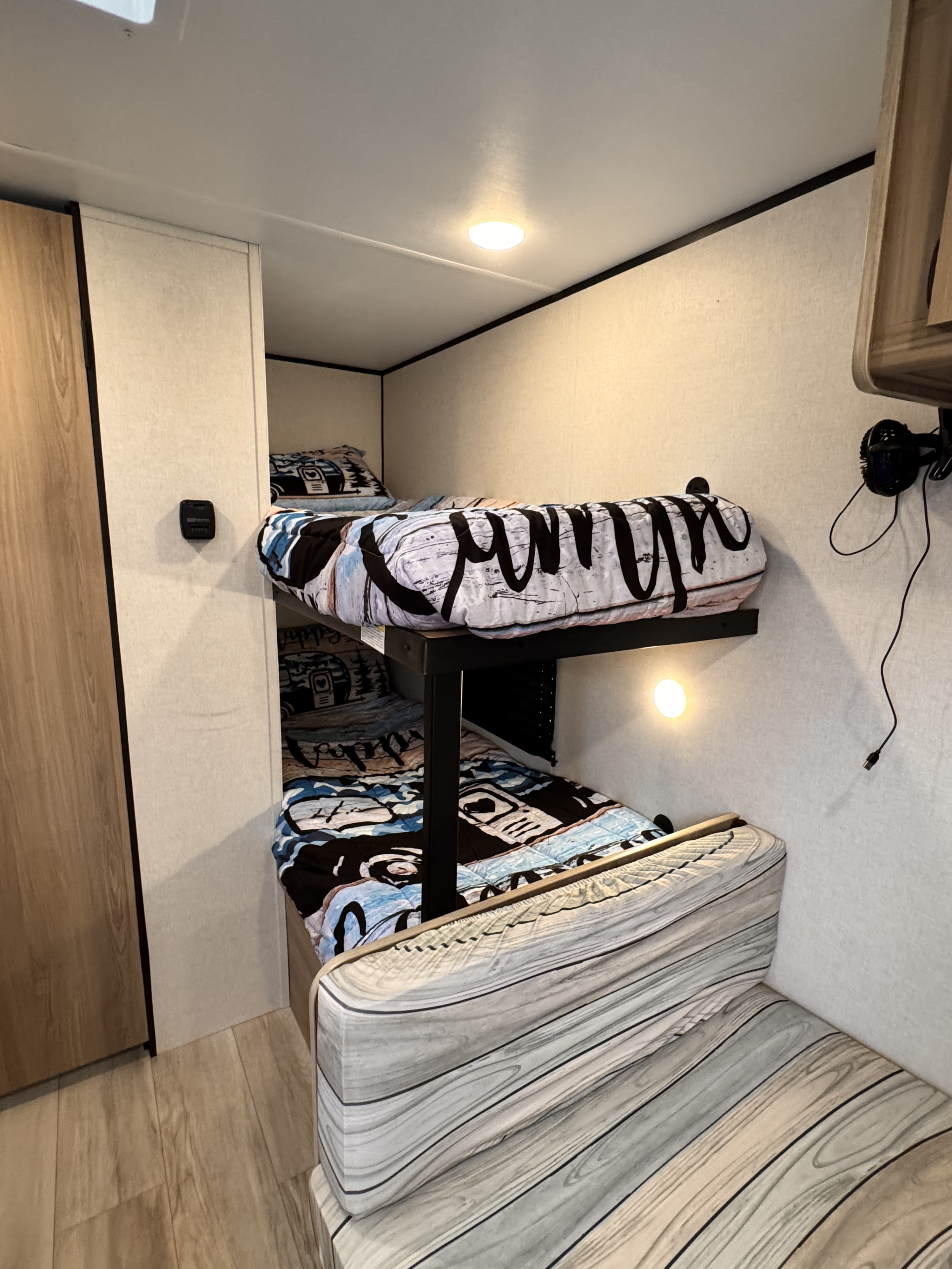 RV rental interior showing two levels of bunk beds with themed bedding, a wall light, and charging cable.. Keystone Coleman 17B 2025