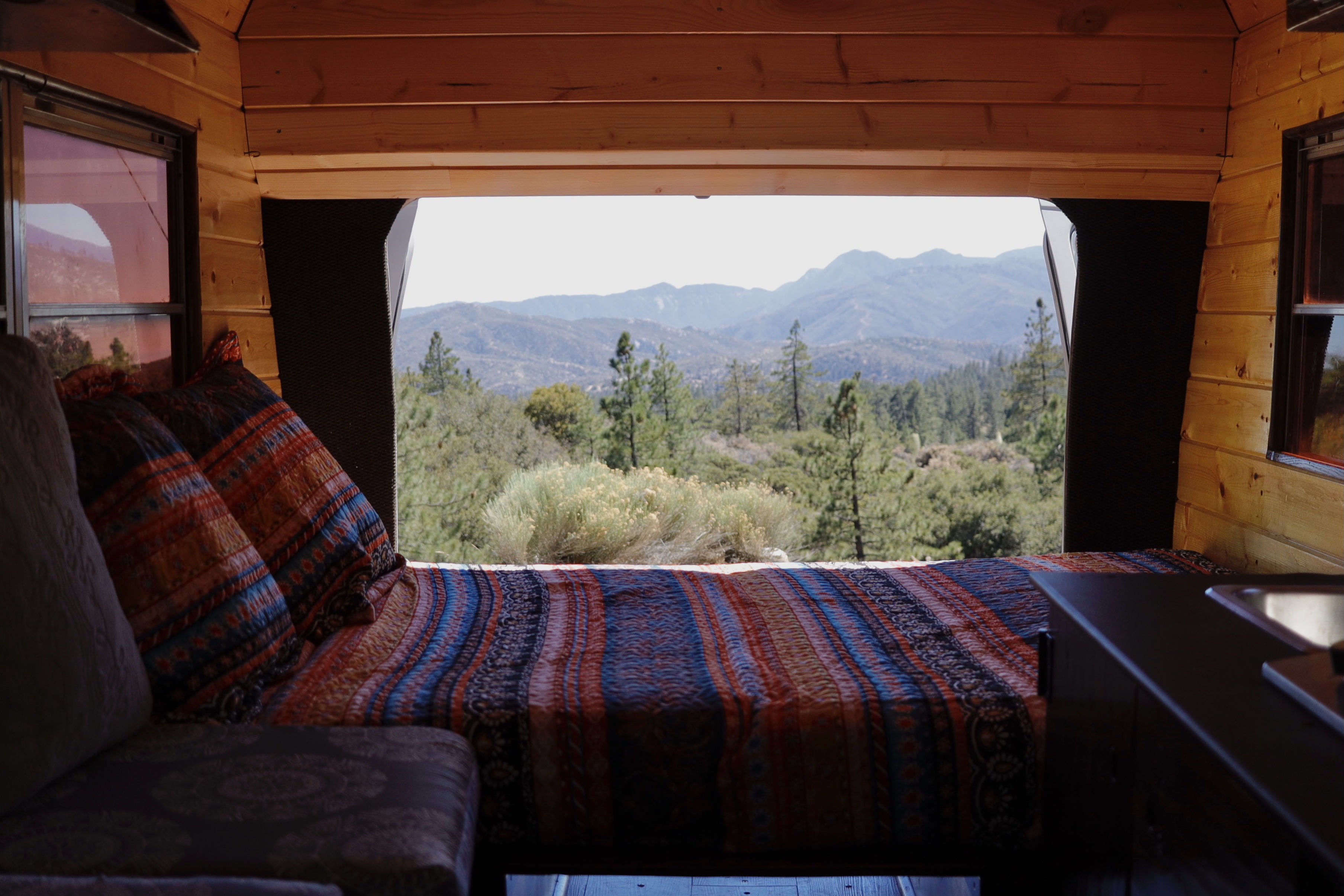 Cozy RV rental interior with a colorful bed, pillows, and a stunning mountain and forest view. Perfect for travel.. Ford Econoline 1989