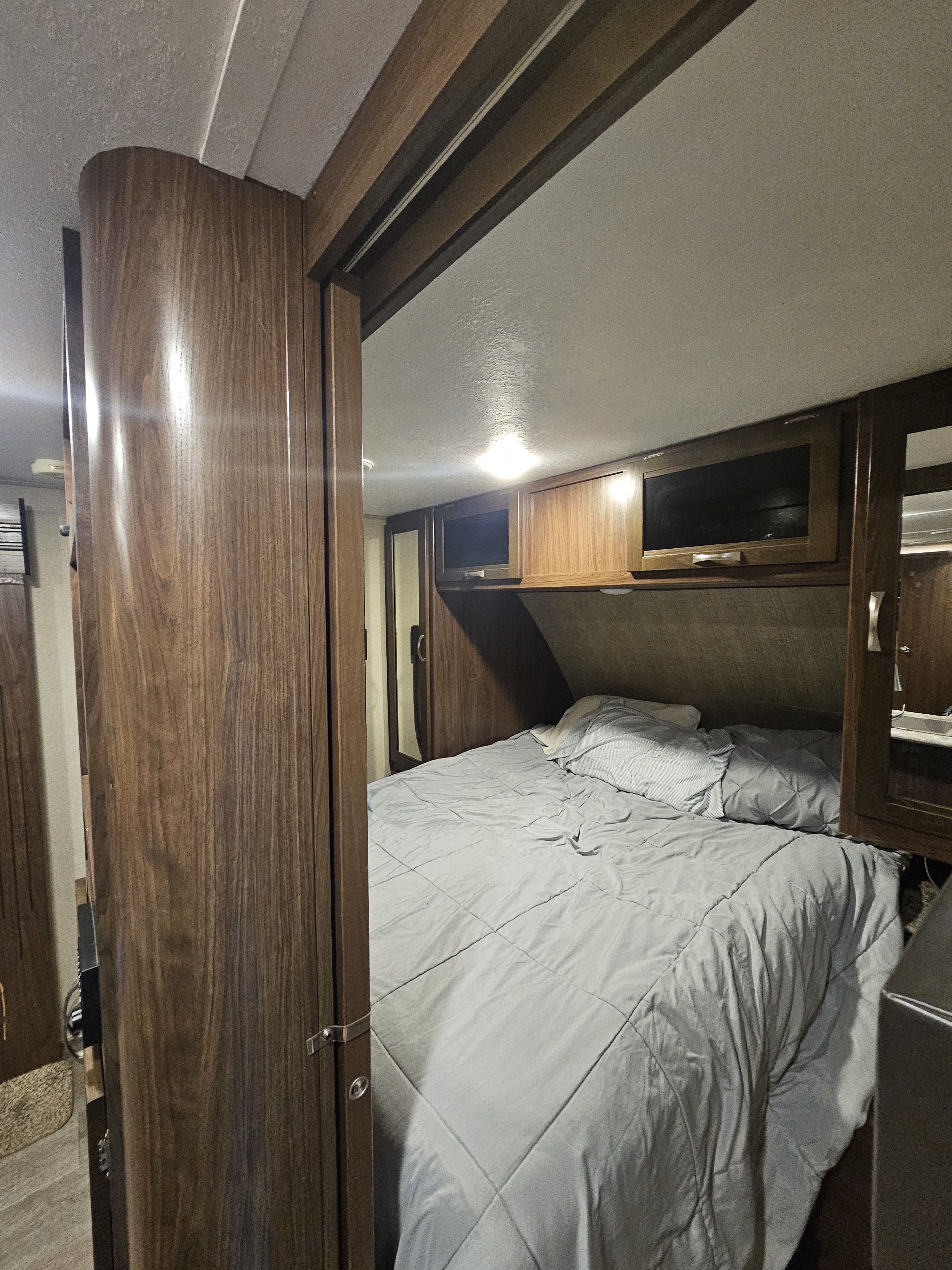 Experience comfort in this RV rental bedroom featuring a bed, overhead cabinets, and warm wood finishes.. Dutchmen Coleman Light 2018