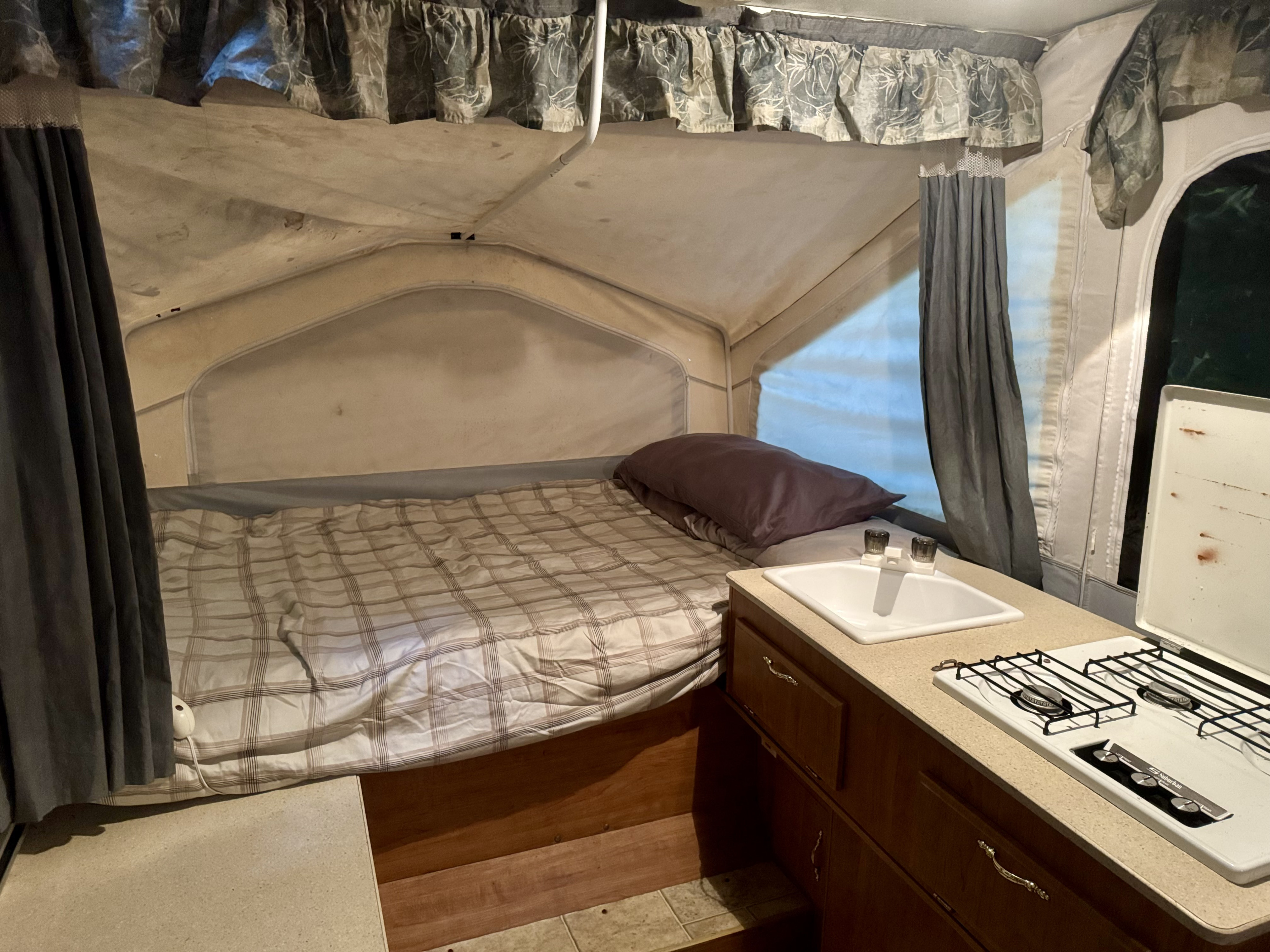 Step inside this RV rental, featuring a comfortable bed with plaid sheets, a sink, and a two-burner stove, ready for adventure.. Forest River Flagstaff Off Road 2006