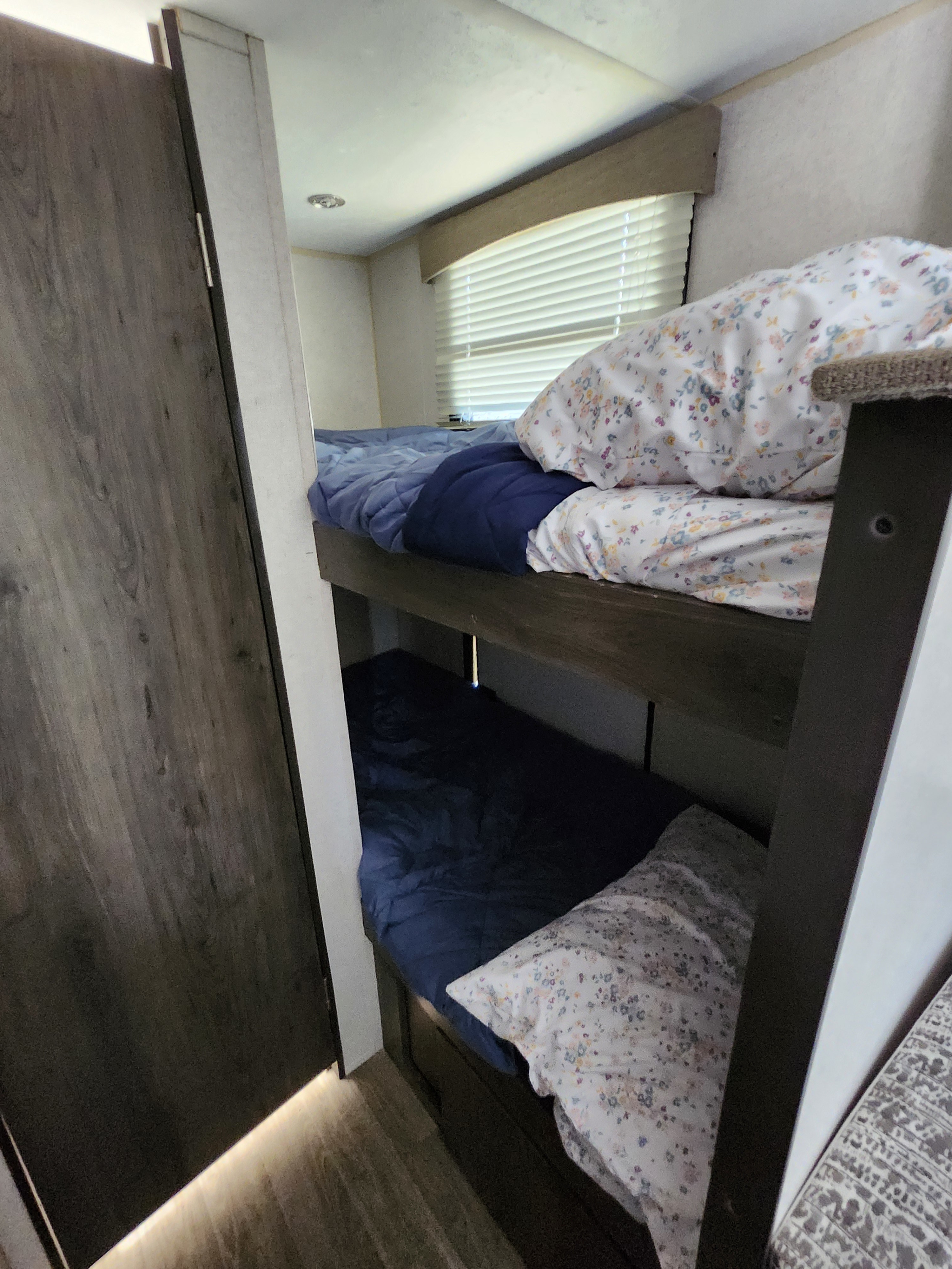 Cozy RV rental bunk beds featuring floral pillows, blue bedding, and window blinds for comfortable rest.. Forest River Viking 2020