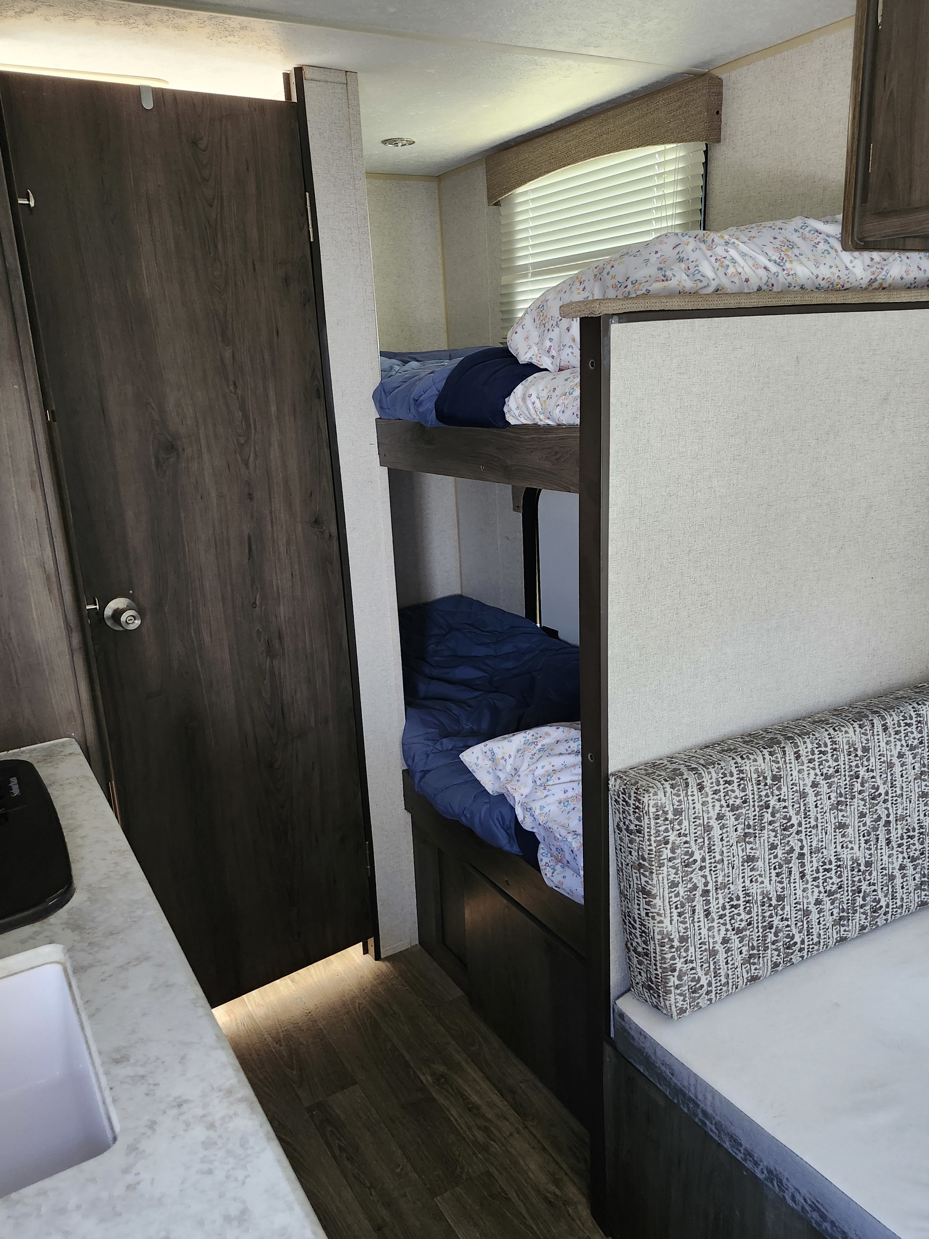 This RV rental shows bunk beds with patterned bedding, a dinette, a sink counter, and a dark wood door inside.. Forest River Viking 2020