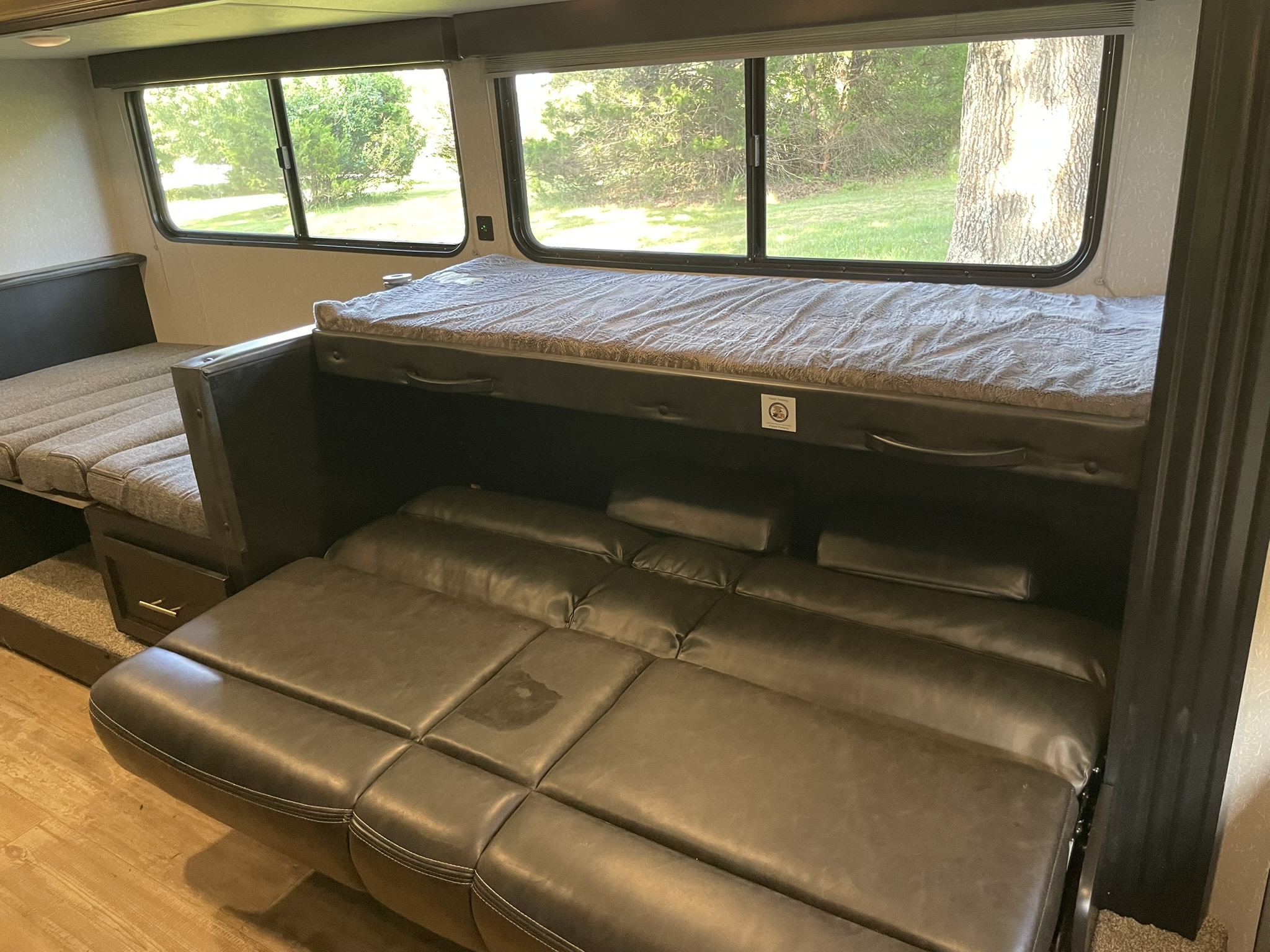 RV rental interior featuring a convertible sofa and bunk bed, with bright windows showing outdoor greenery.. Forest River Cherokee Wolf Pup 2021