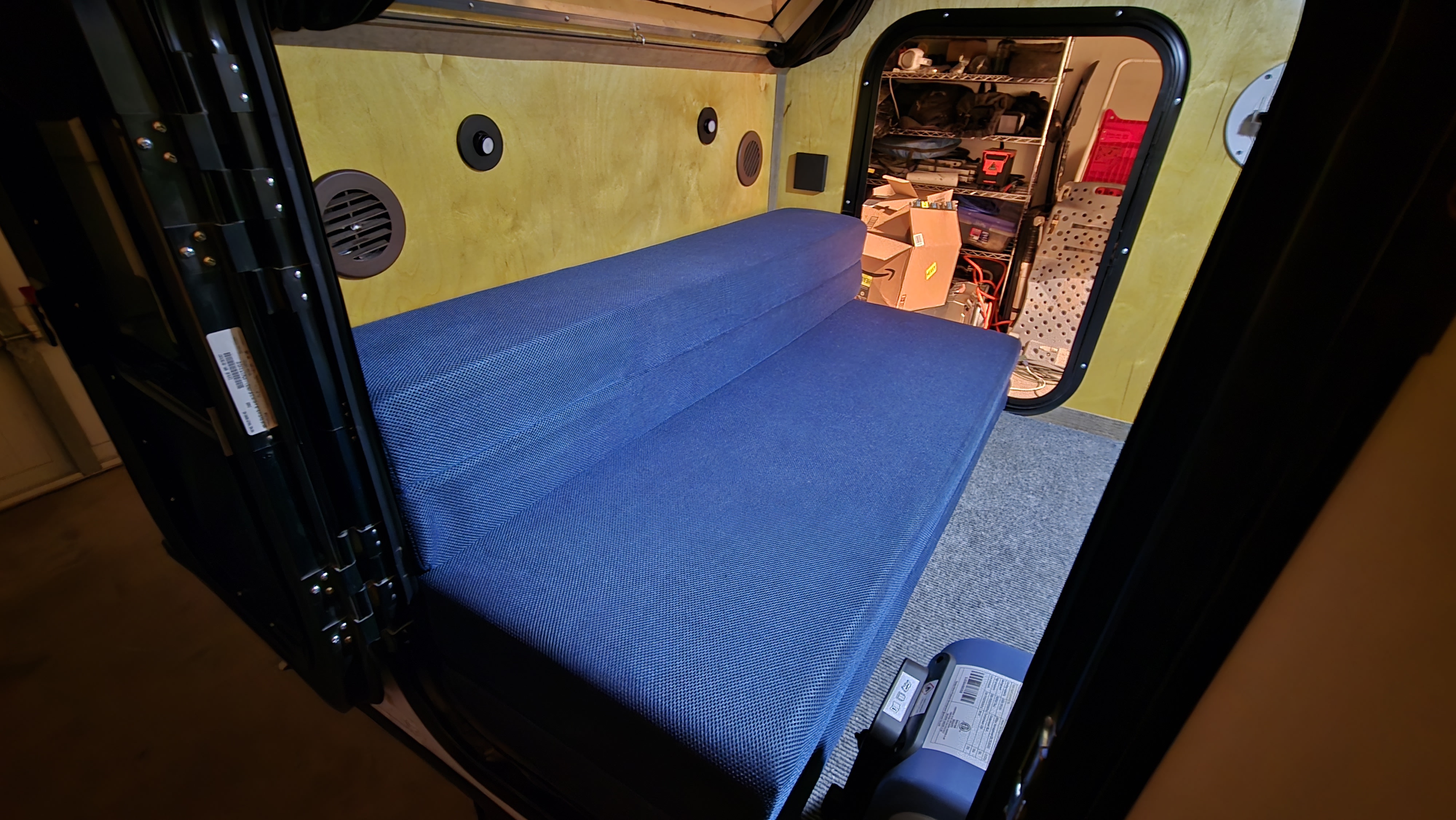 RV rental: Interior of a small camper with a blue folding mattress, wood-paneled walls, and organized rear storage.. Venture Overland Campers XTR OFFROAD 2024