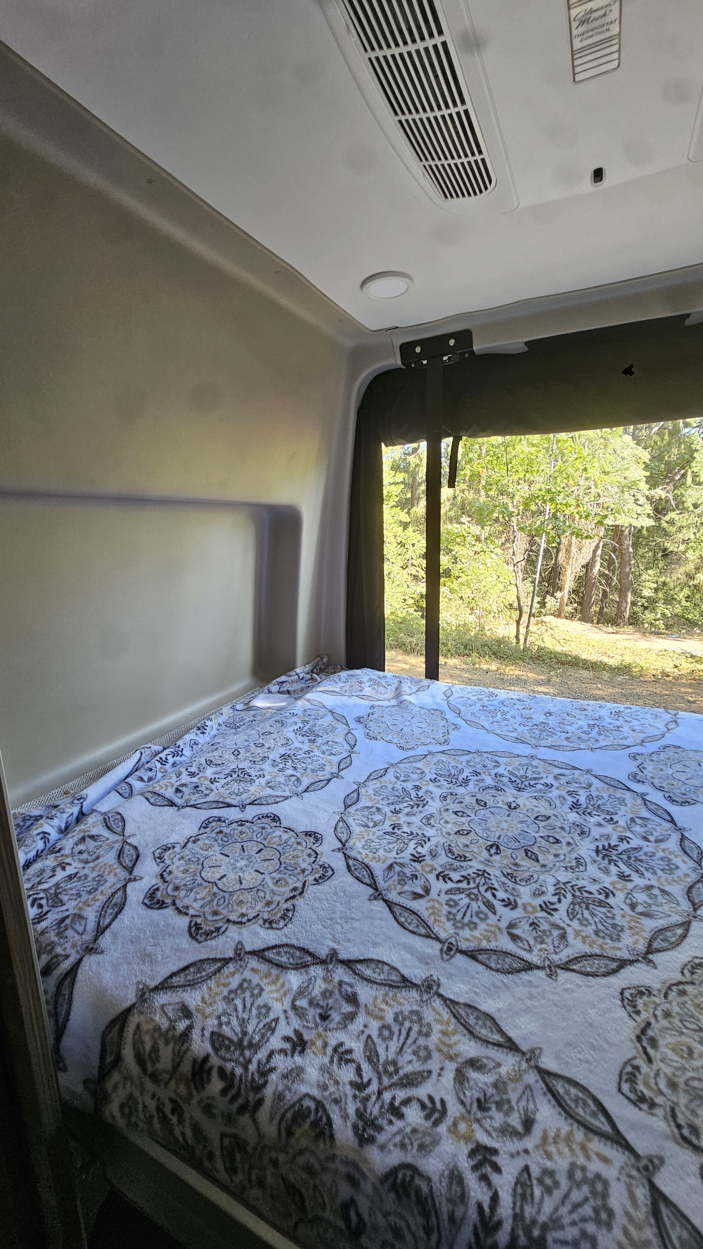 RV rental interior: cozy bed with a patterned blanket, looking out to a lush forest scene.. Jayco Terrain 2024