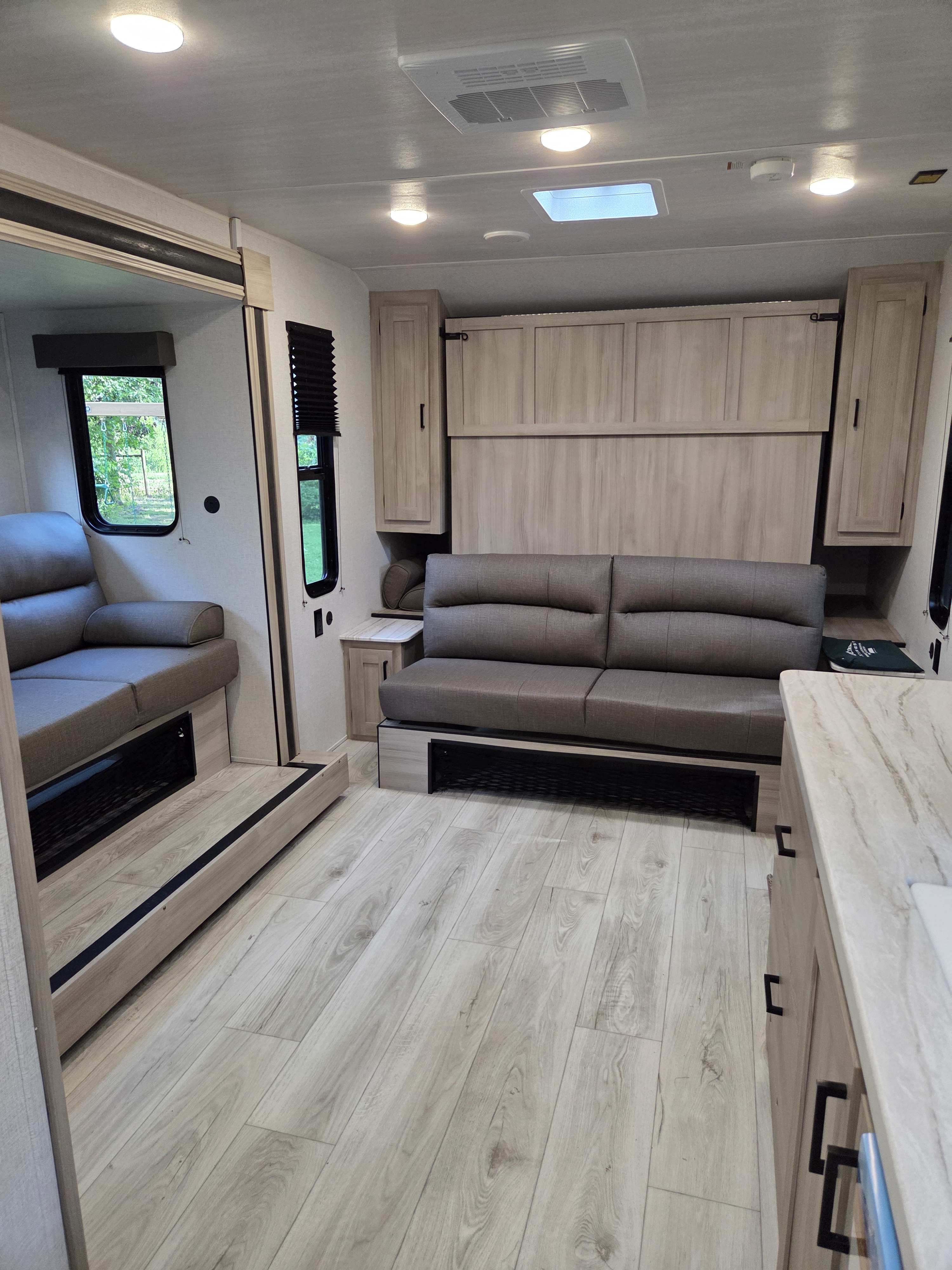 Modern RV rental interior featuring light wood flooring, a comfortable gray sofa, and integrated kitchen amenities. Bright and spacious.. Forest River Silver Lake 1800RB 2025